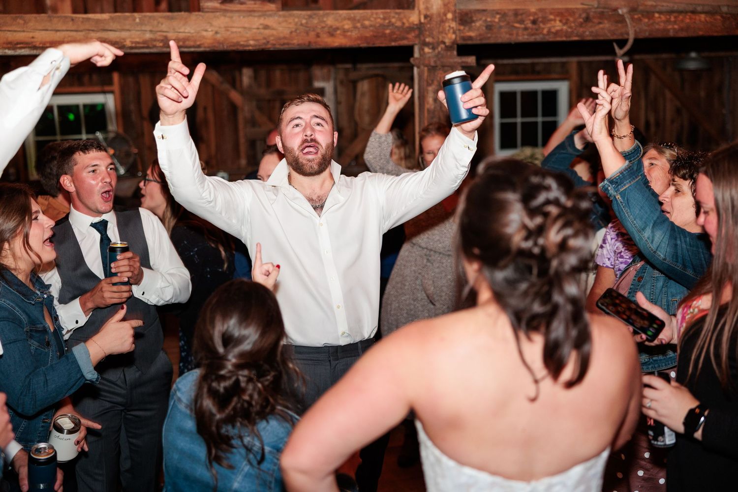 Wedding reception party guests dancing and celebrating in a rustic barn venue.