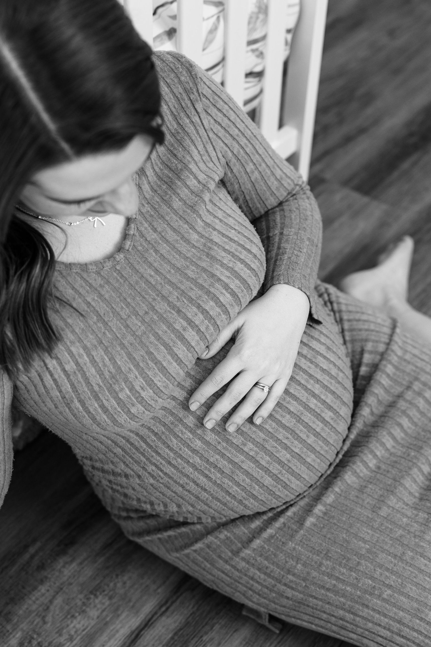 Black and white overhead view of a pregnant woman in a ribbed dress gently cradling her baby bump.