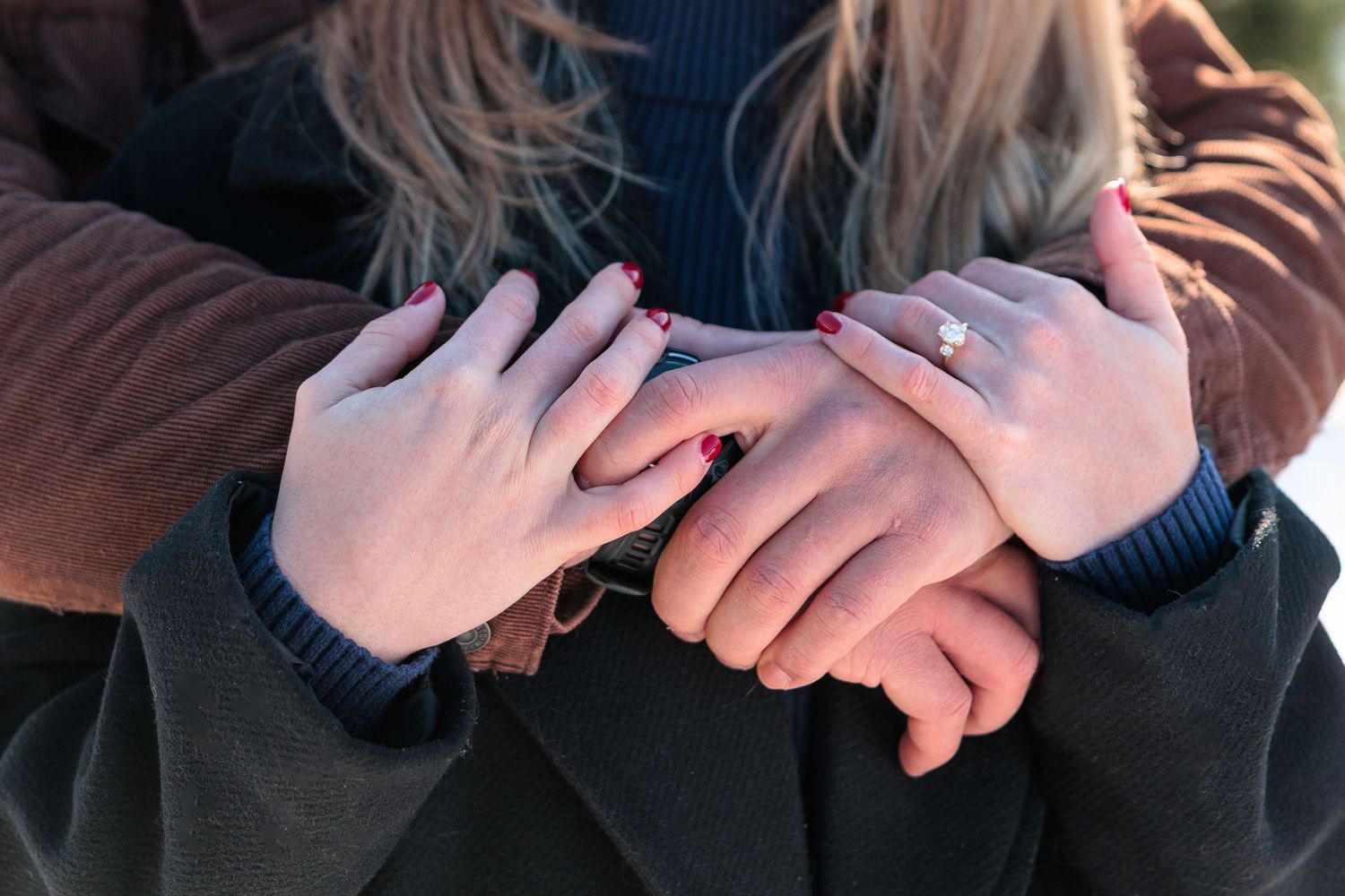 Close-up of couple's hands showing engagement ring with pink manicured nails outdoors.