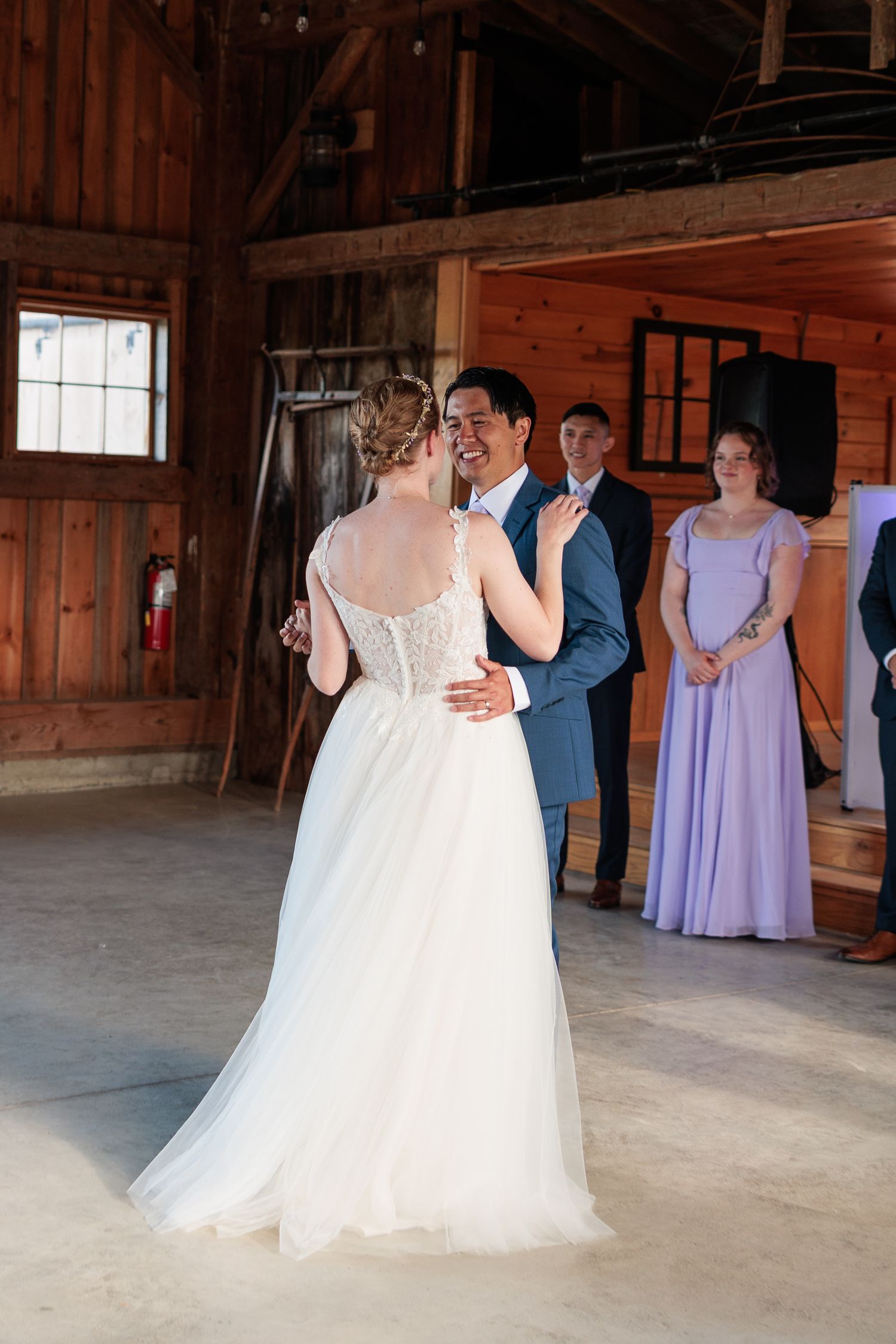 Couple shares first dance in warmly lit rustic barn as guests look on.