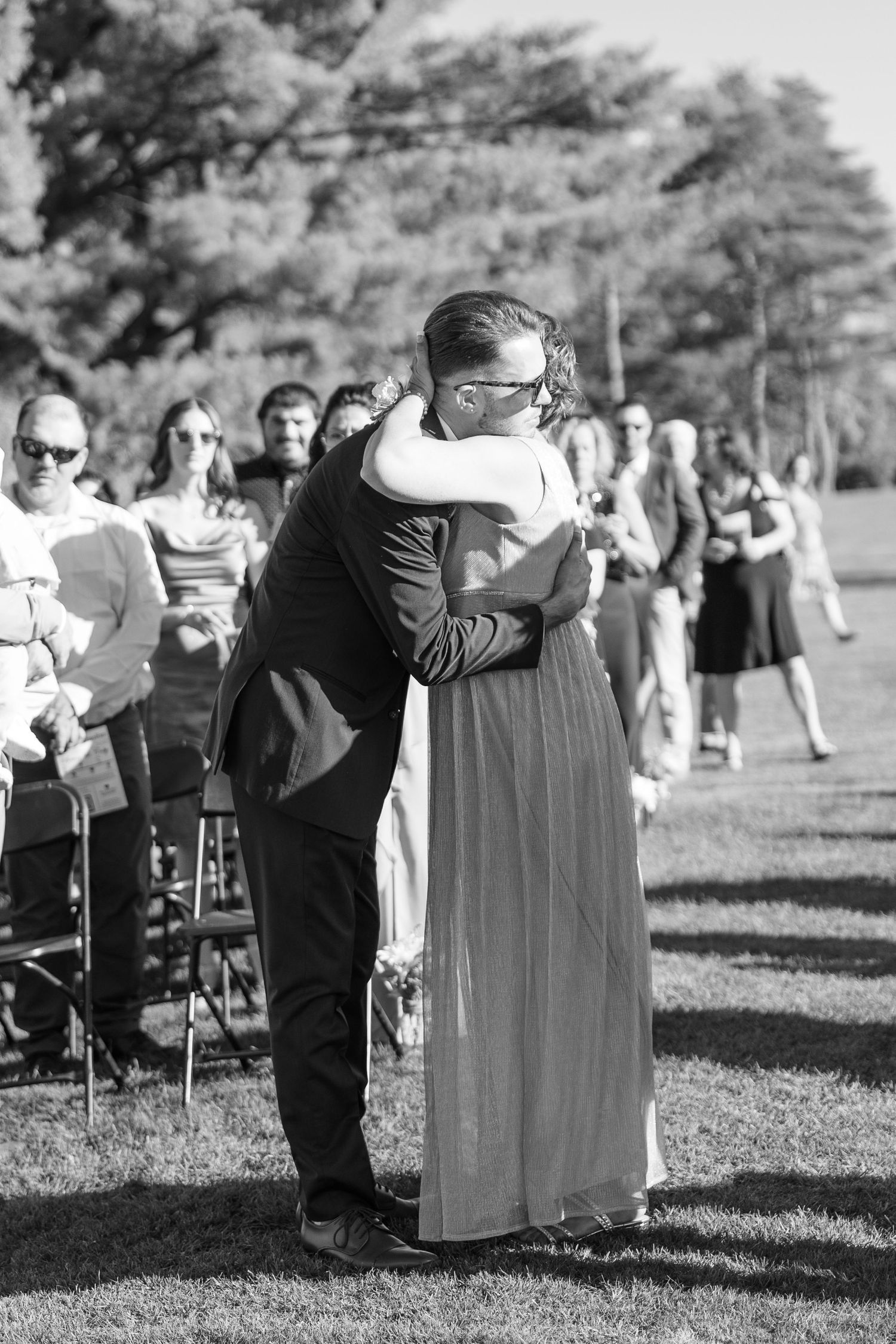 Wedding ceremony guests gathered outdoors in formal attire.