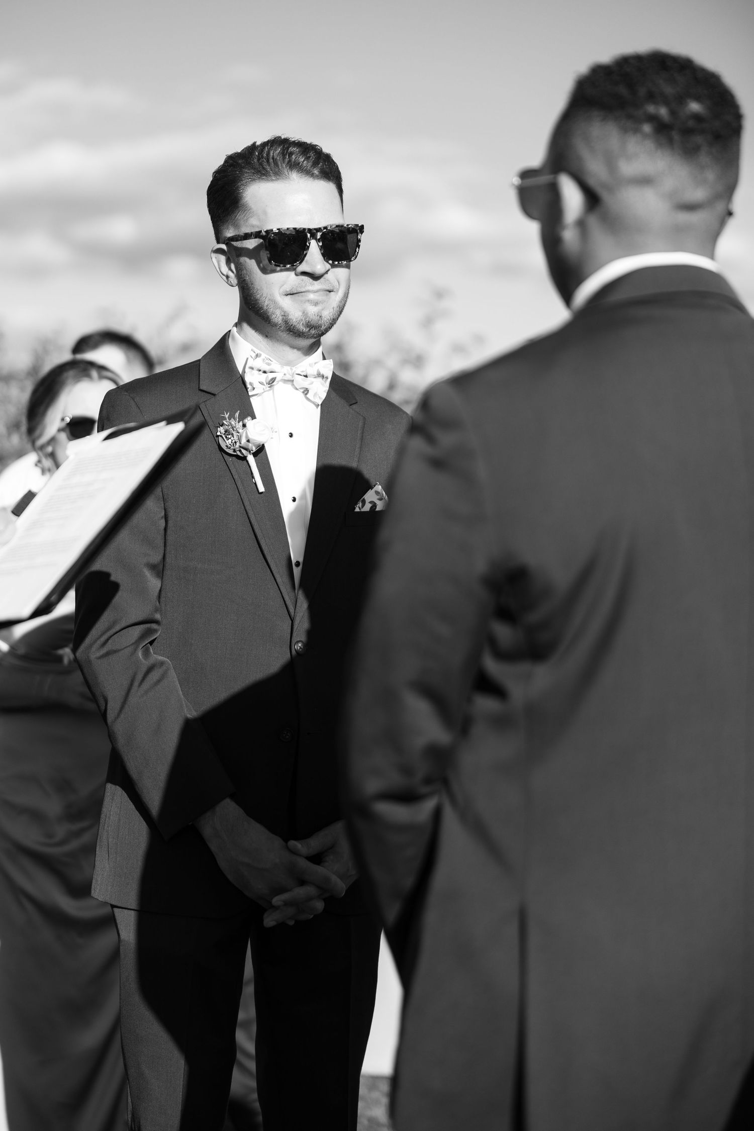 Groomsmen in formal black tuxedos and bow ties gathered during wedding ceremony.