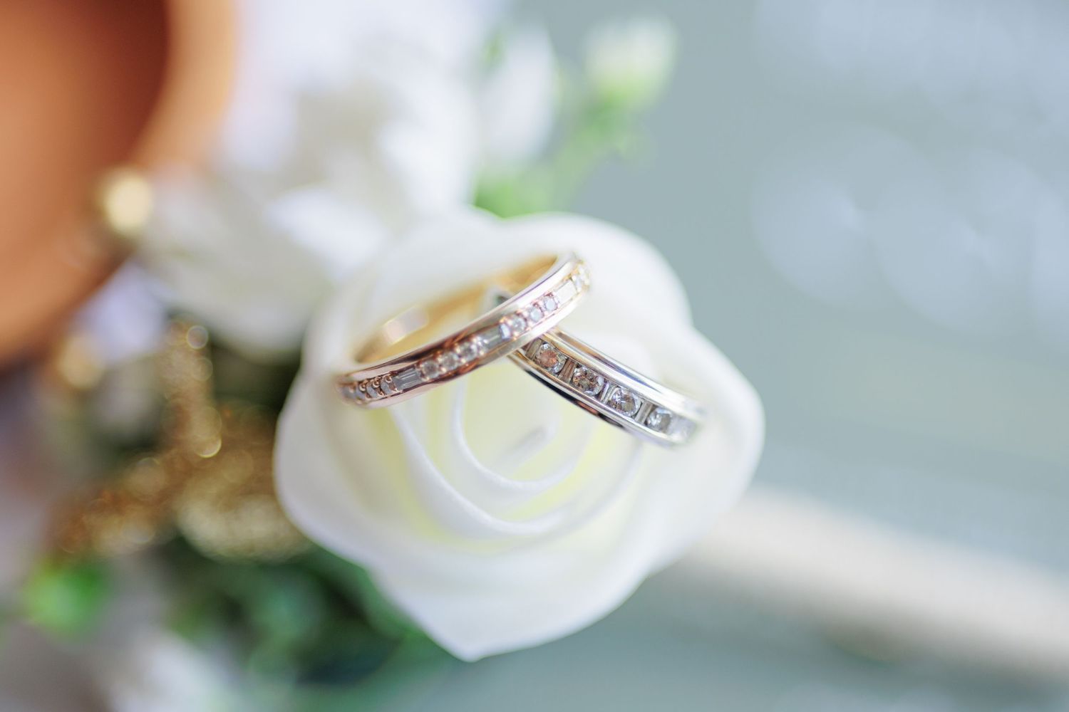 Elegant wedding rings displayed on white roses with delicate greenery accents.