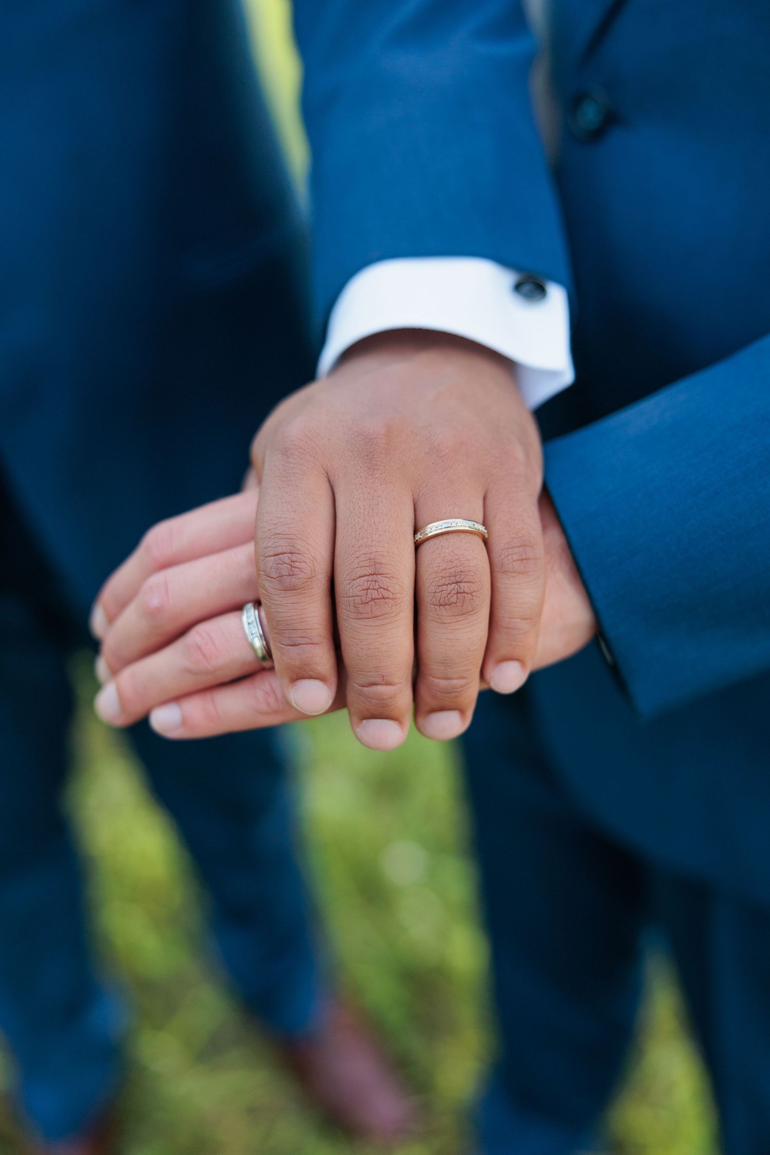 Close-up shots of hands wearing wedding rings against navy blue suit backgrounds.