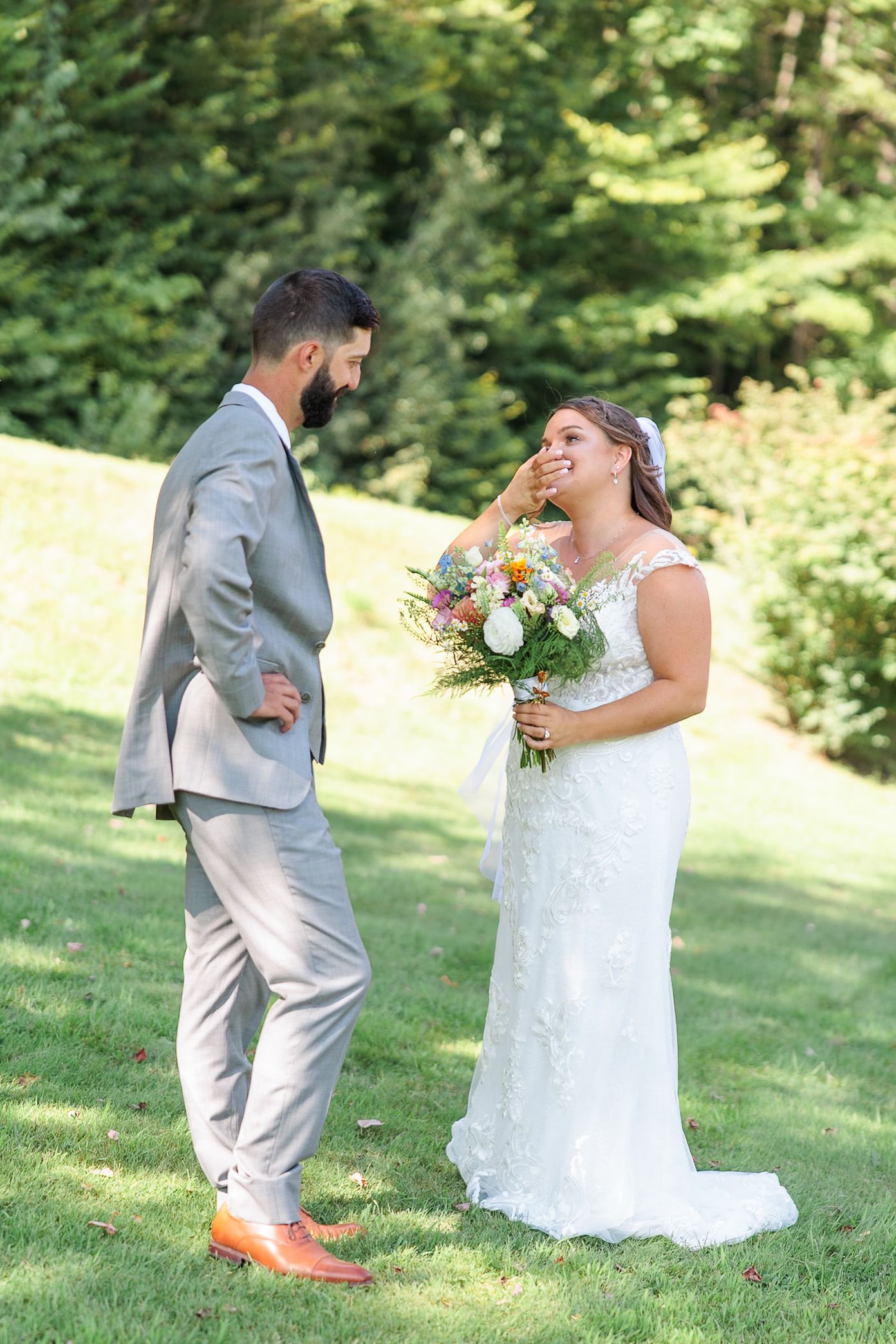 Bride and groom share joyful first look moment on sunny green lawn.