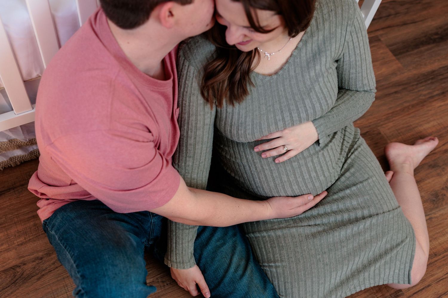 Overhead view of a couple sitting on a wooden floor, both tenderly holding the pregnant woman's belly.