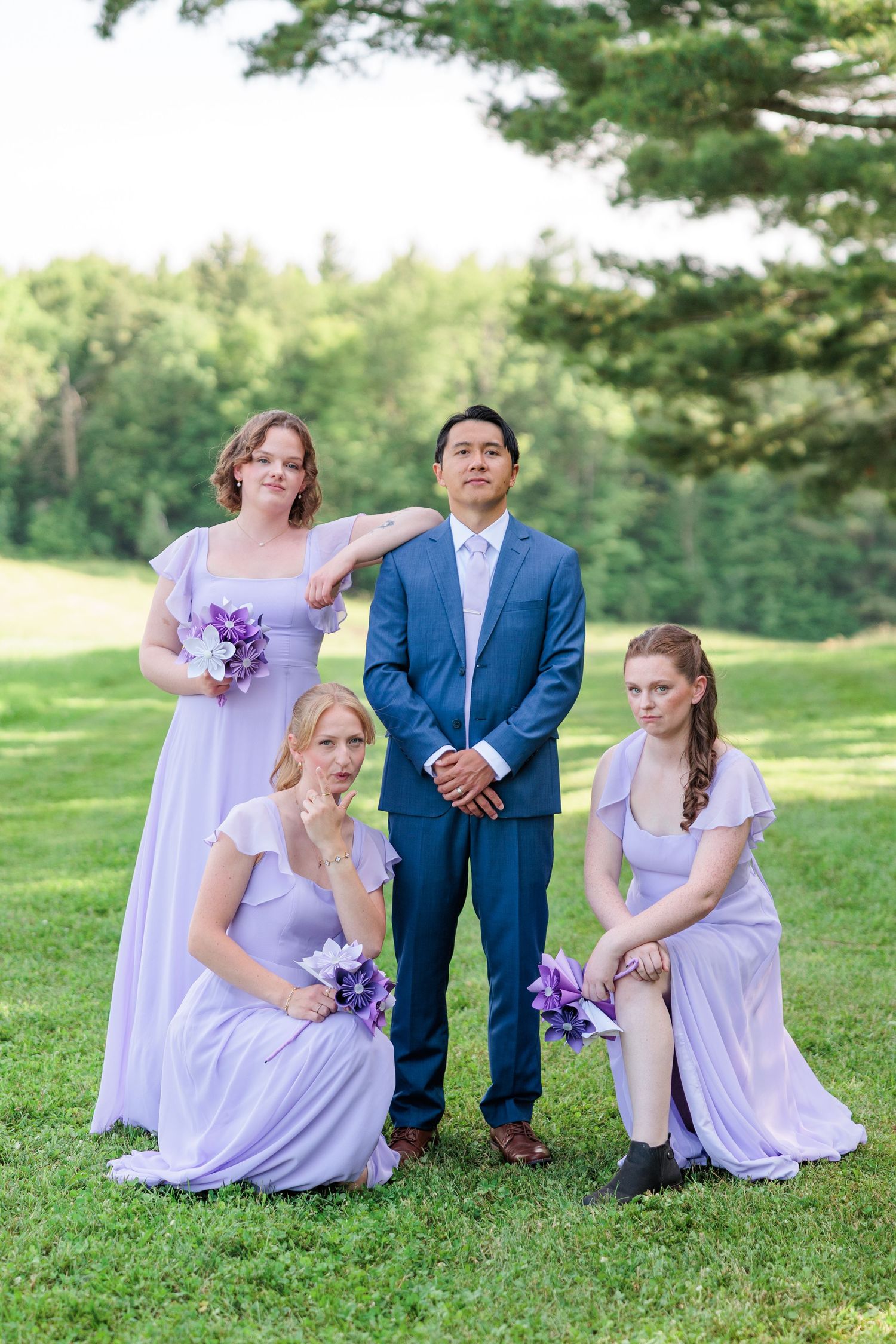 Groom in blue suit posing with three bridesmaids in lavender dresses making funny faces.