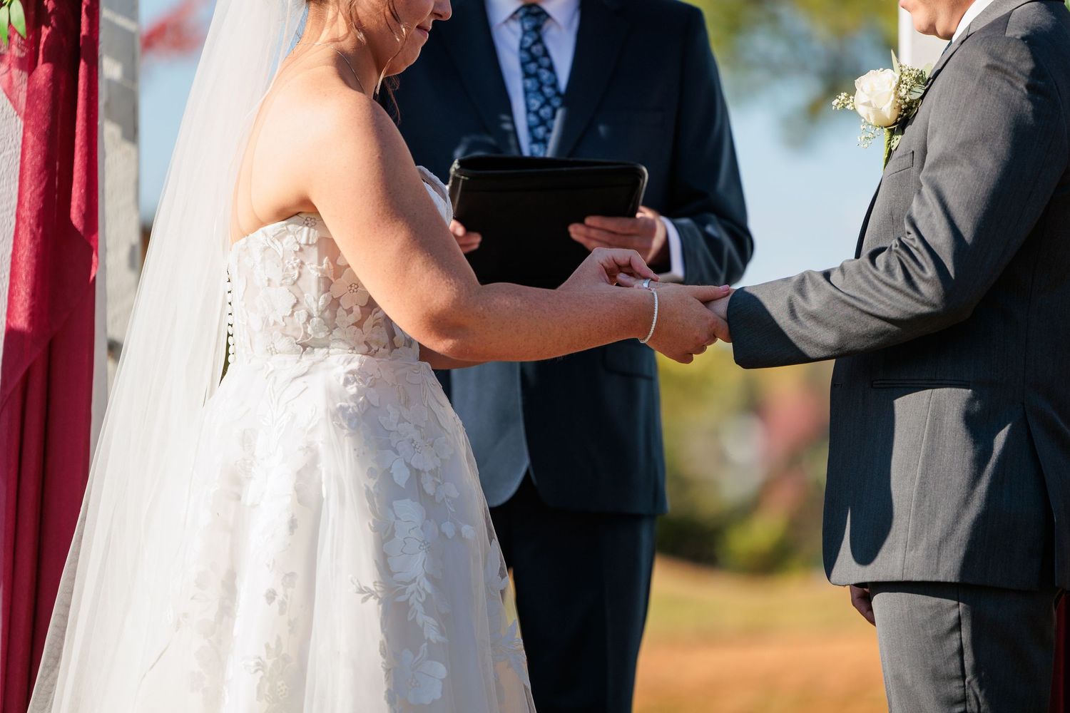 Wedding ceremony taking place outdoors with fall foliage in the background.