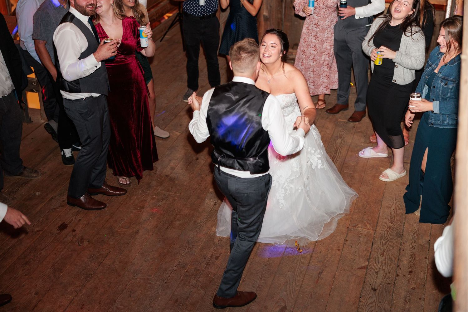 Wedding reception dance party in a rustic barn venue with wooden floors and festive lighting.