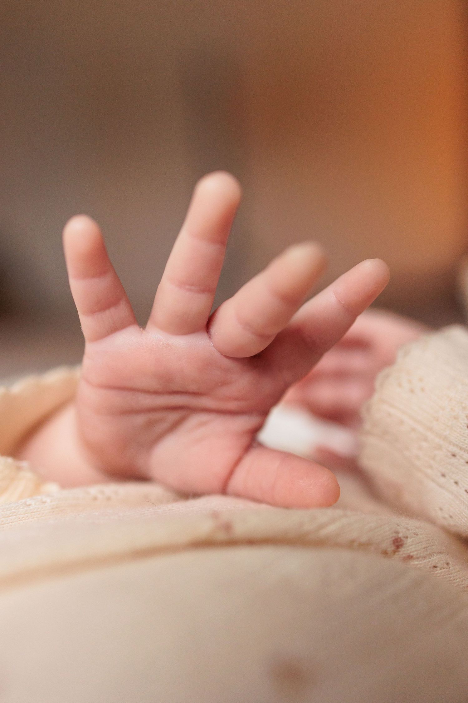 Close-up of a tiny baby hand reaching out against a soft cream-colored background.
