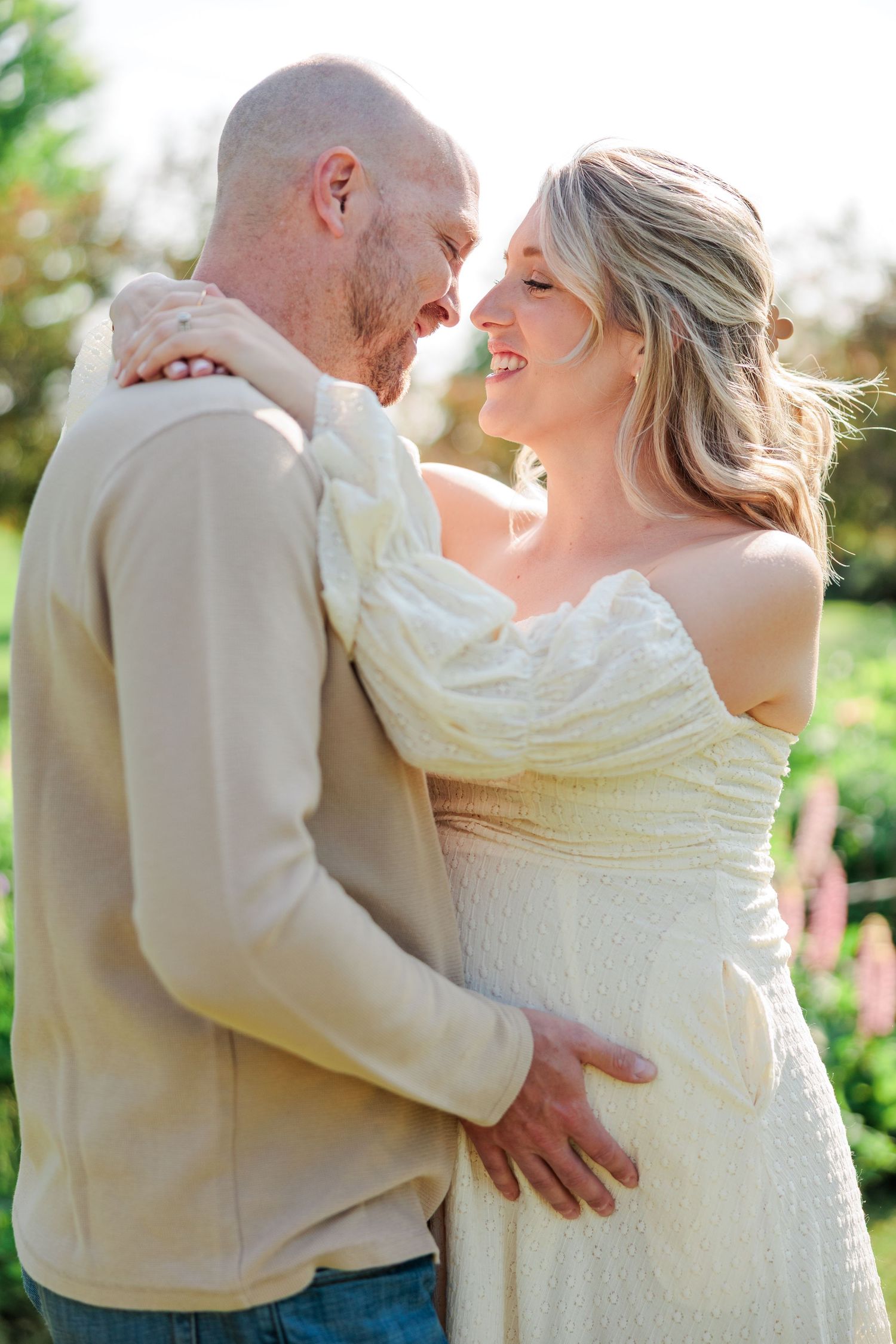Happy couple sharing an intimate moment, pregnant woman in white dress embracing partner in garden.