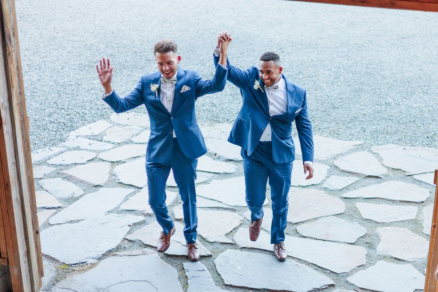 Playful groomsmen jumping in blue suits on stone pathway during wedding photoshoot.
