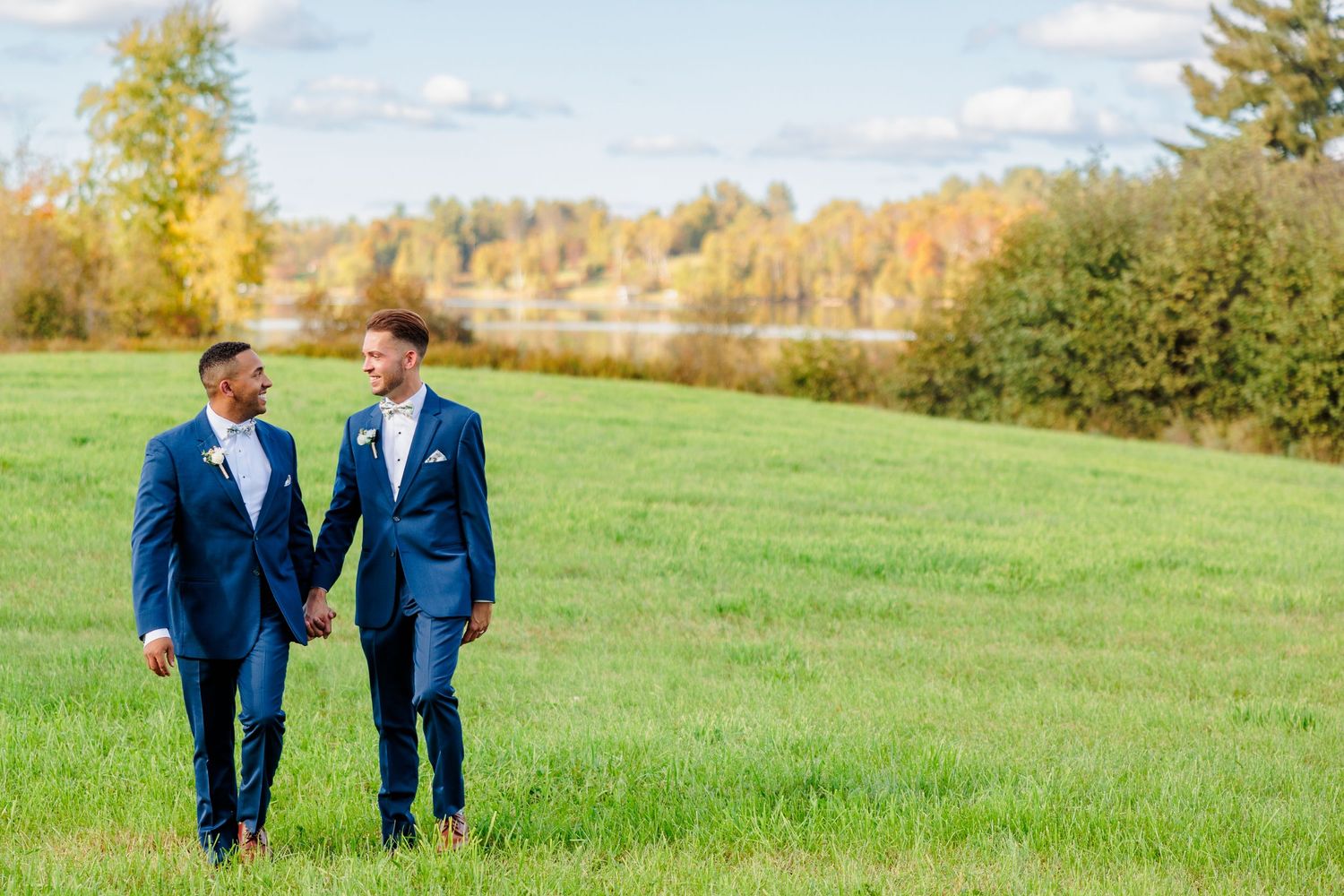 Couple walking hand in hand across sunny autumn field in matching blue suits.