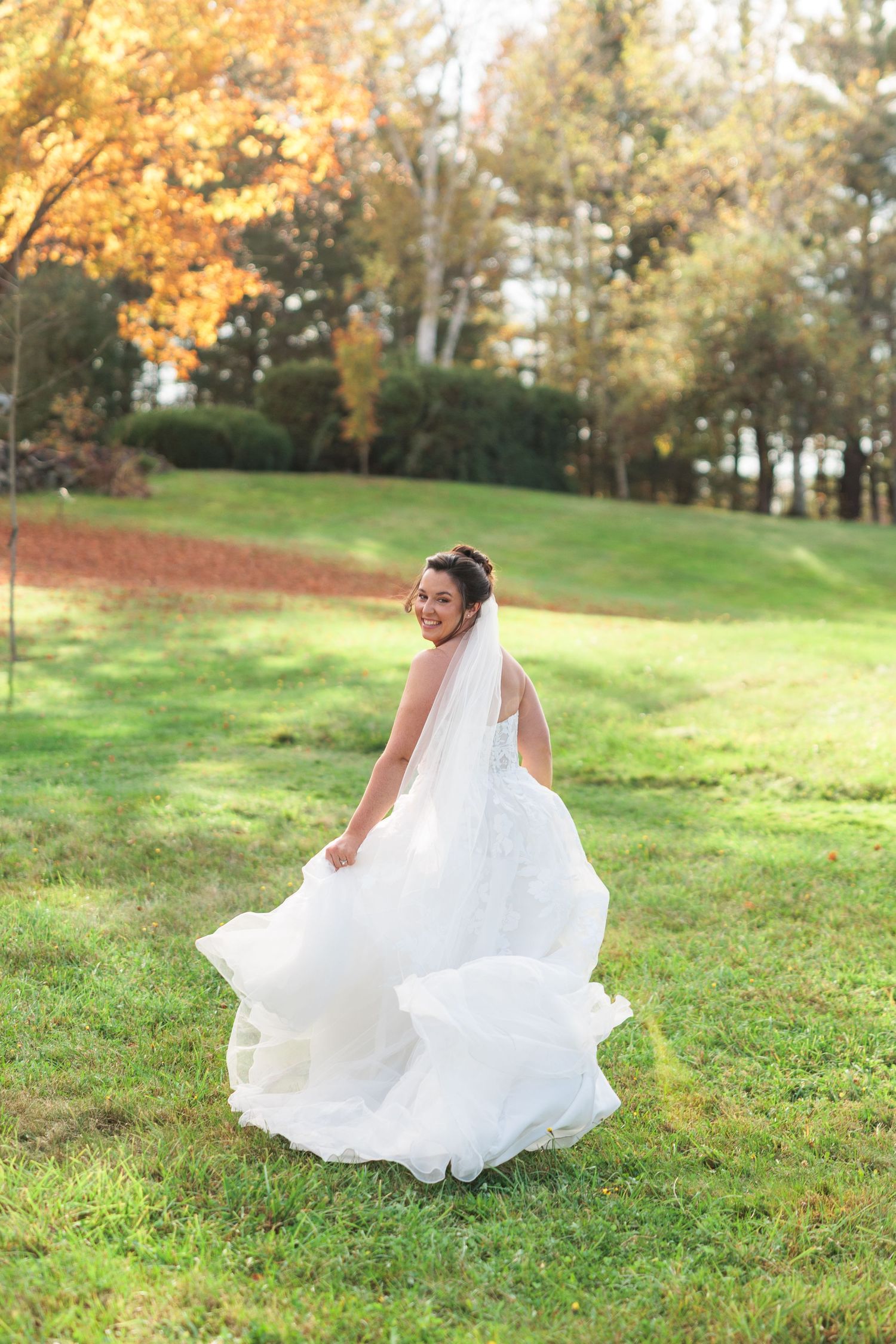 White wedding dress flowing in motion across green grass during autumn photo session.