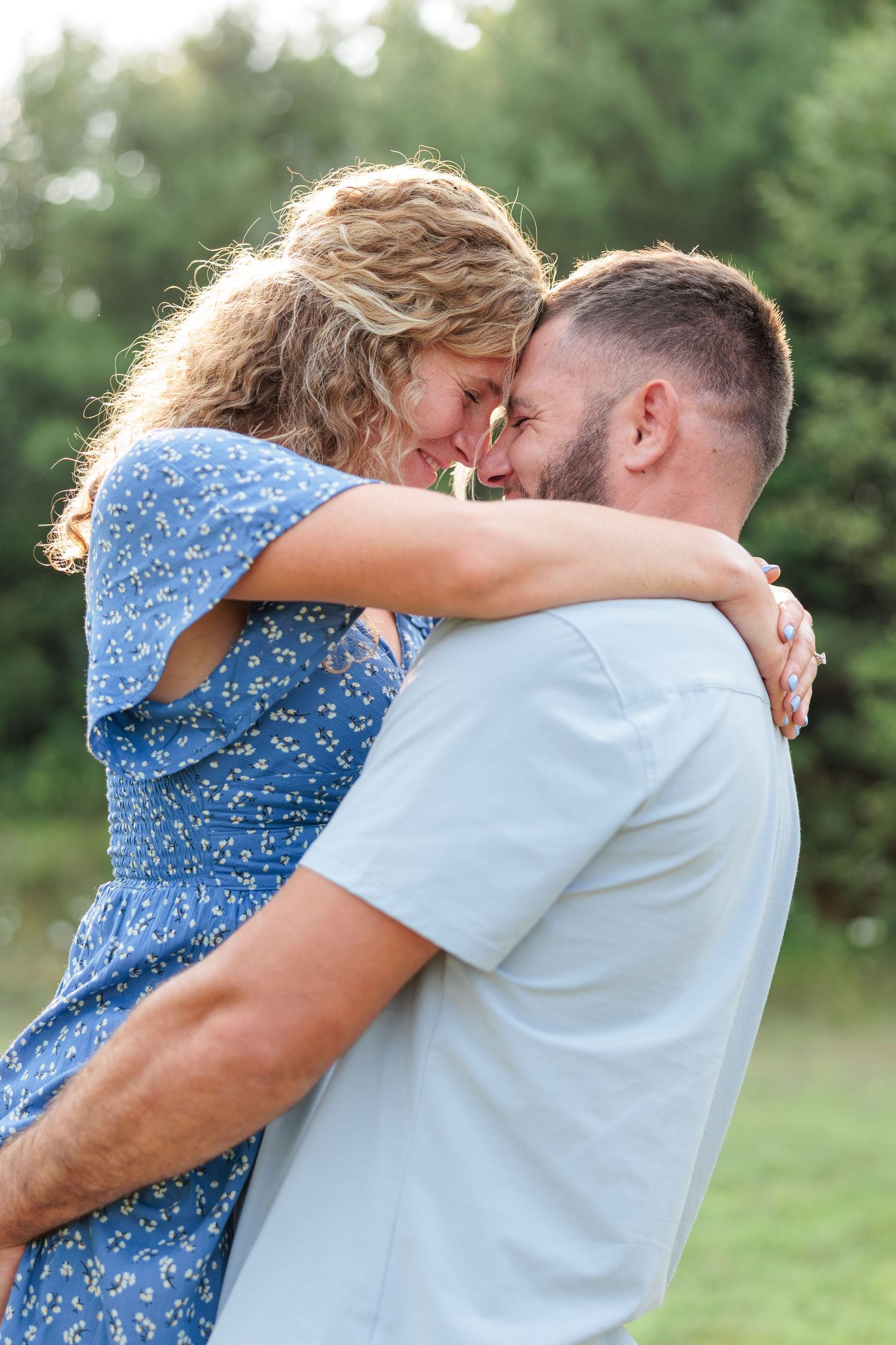 Man lifting and embracing a woman in a blue floral dress in a romantic outdoor couples photo session.