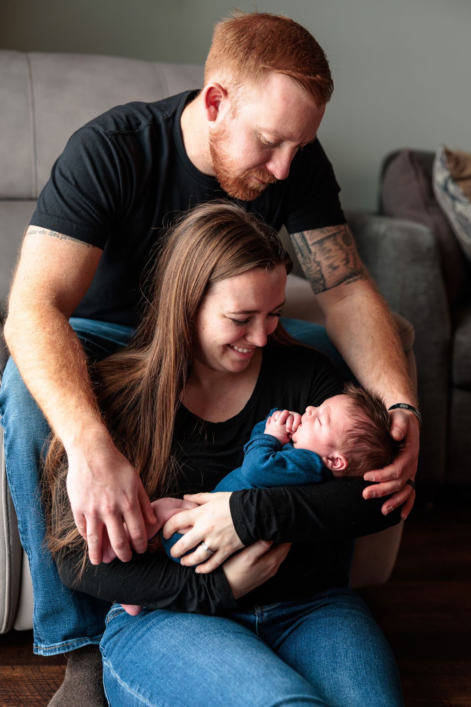 Loving parents with red hair smile down at their newborn baby in a cozy home setting.