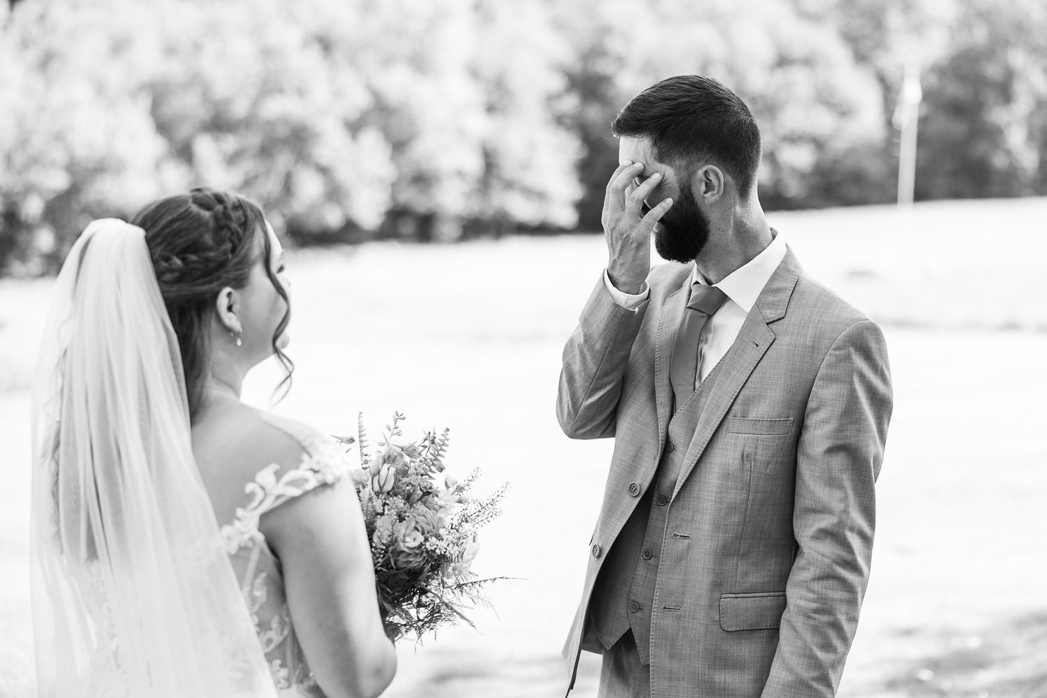 Emotional groom wipes tears during first look with bride in black and white.
