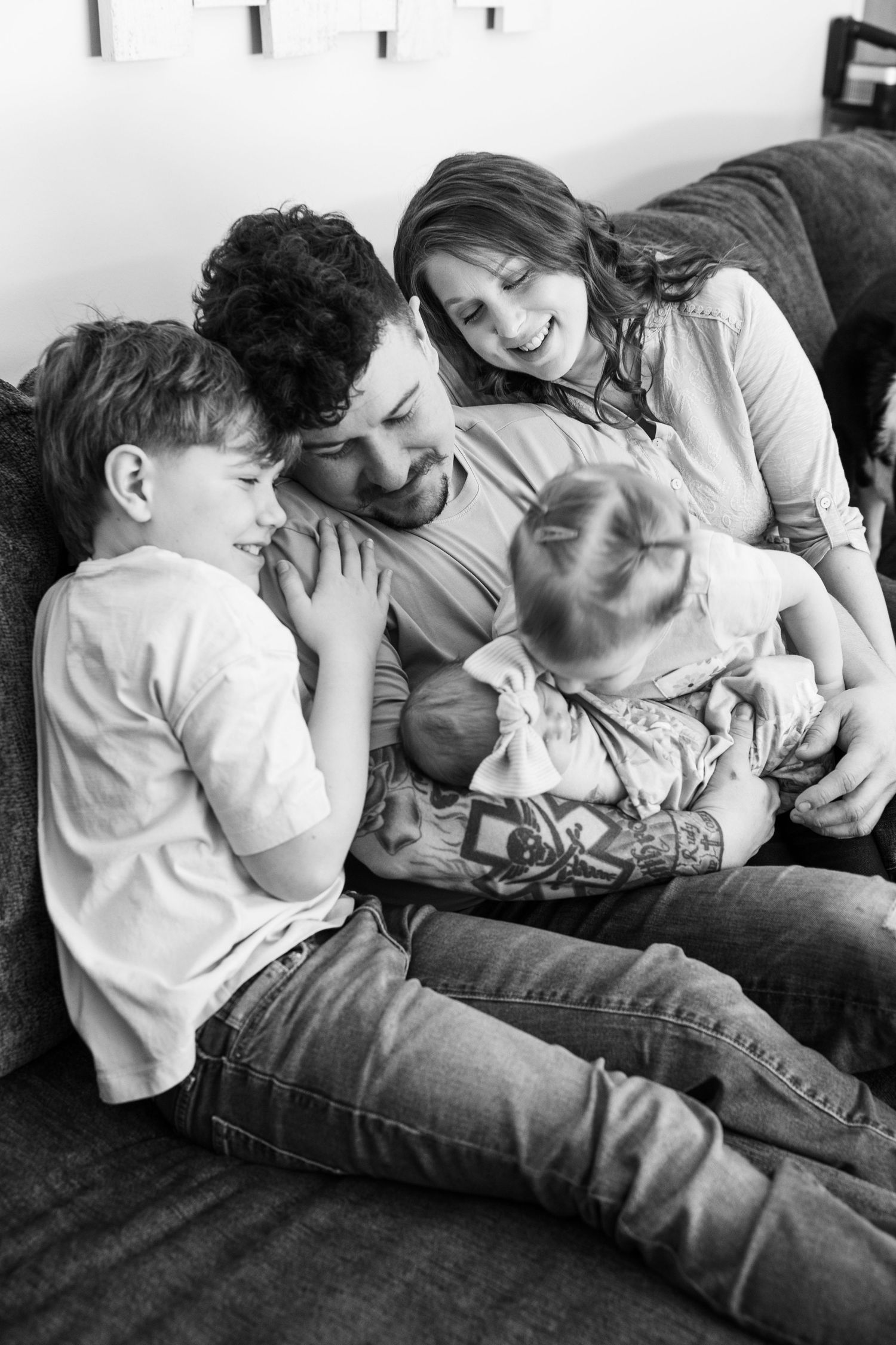 Happy family of four cuddles together on gray sofa in black and white photo.