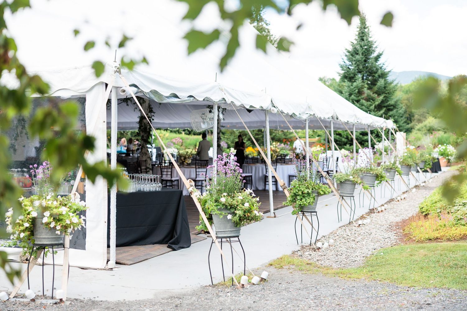 Elegant outdoor wedding reception tent adorned with floral arrangements and black tablecloths at a garden venue.