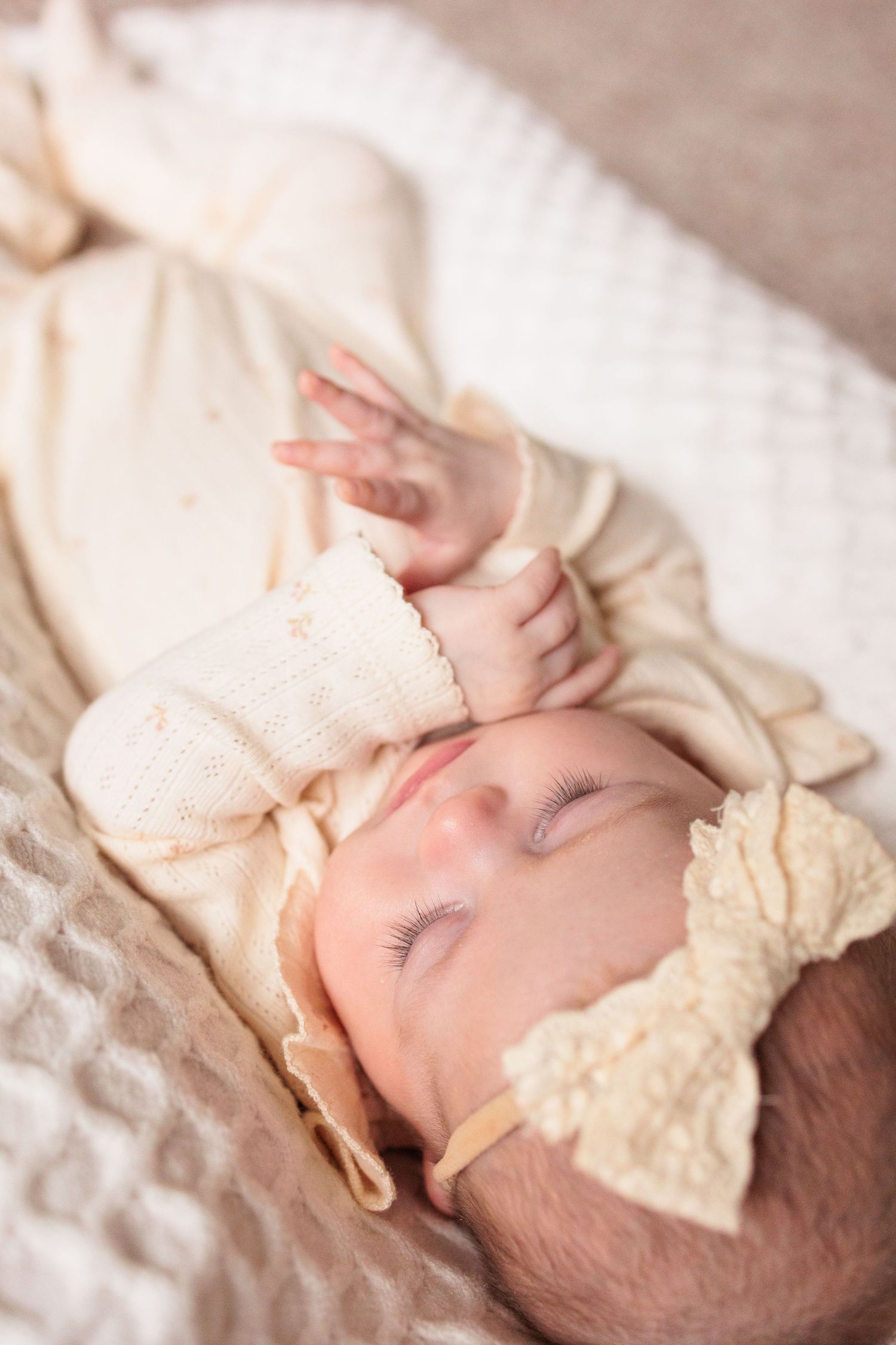 Peaceful sleeping infant in cream knit clothing with soft natural lighting.