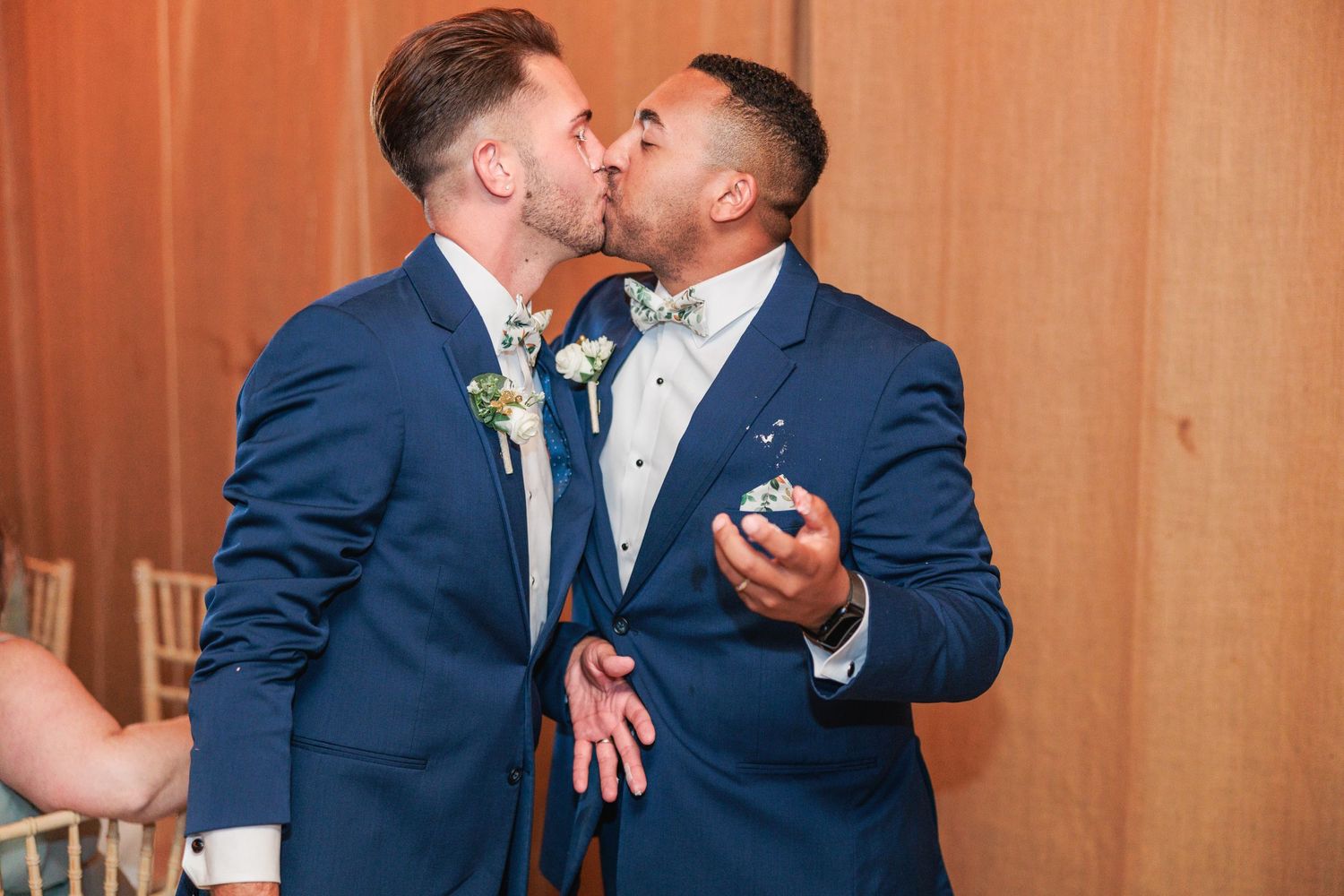 A couple in navy blue suits embrace during their first dance at a wedding reception.