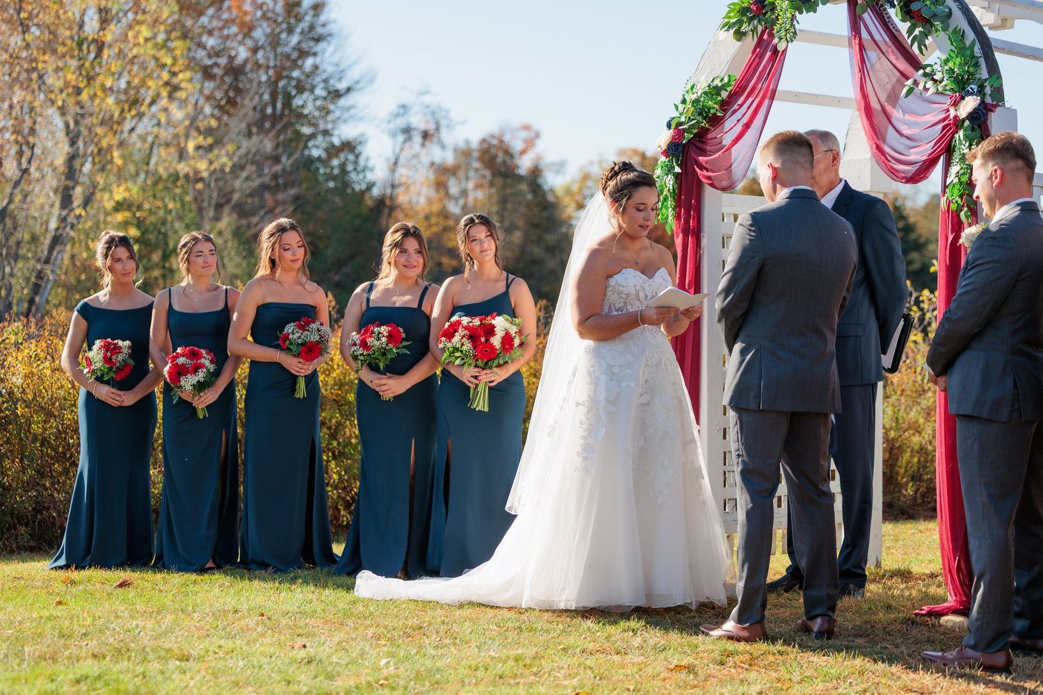 Wedding party in navy blue and white attire posing outdoors against fall foliage.