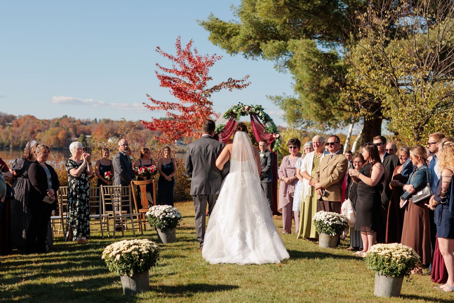 Wedding ceremony setup with rows of wooden chairs on grass under fall foliage.