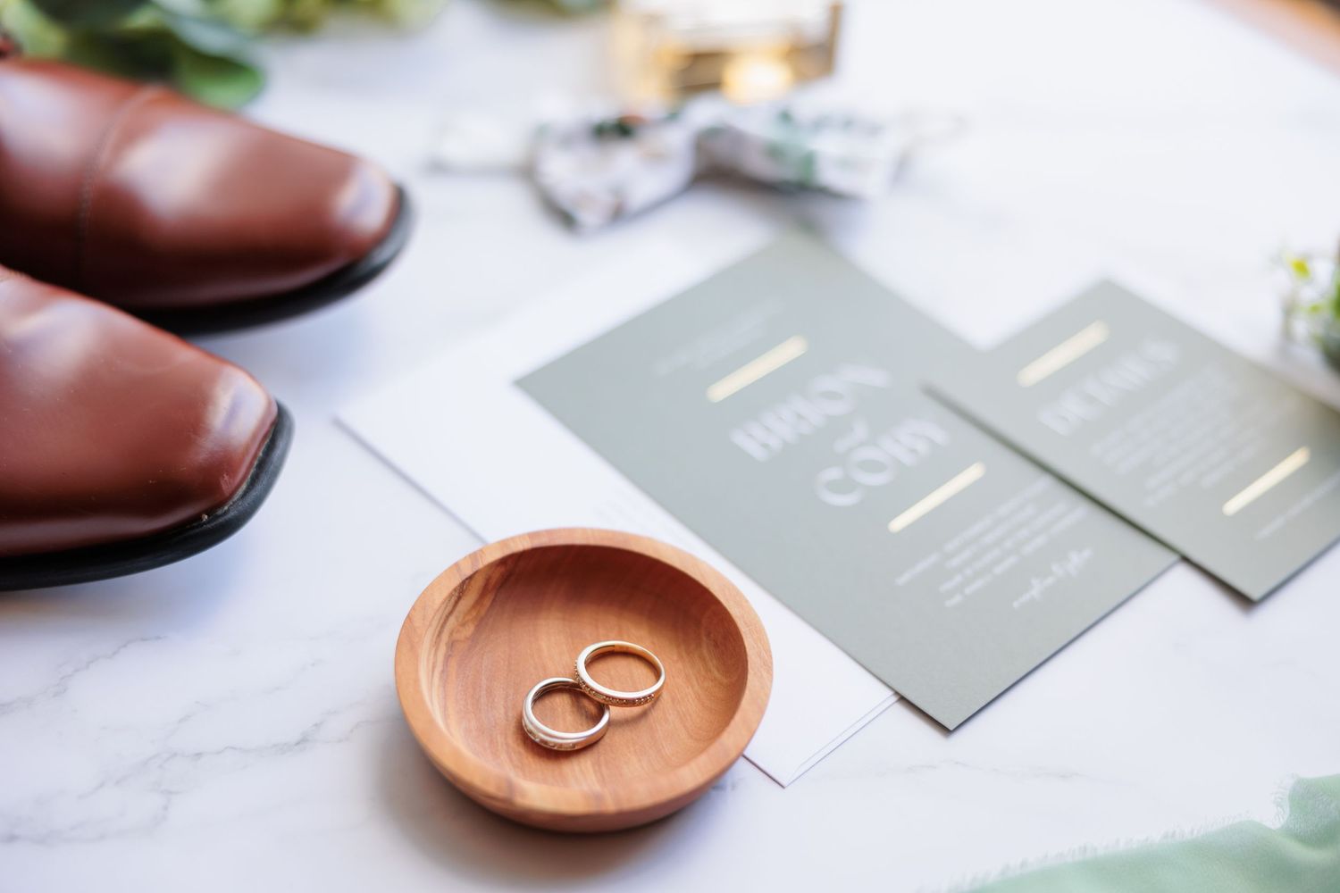 Wedding details featuring wedding rings on a terra cotta dish with elegant gray stationery.