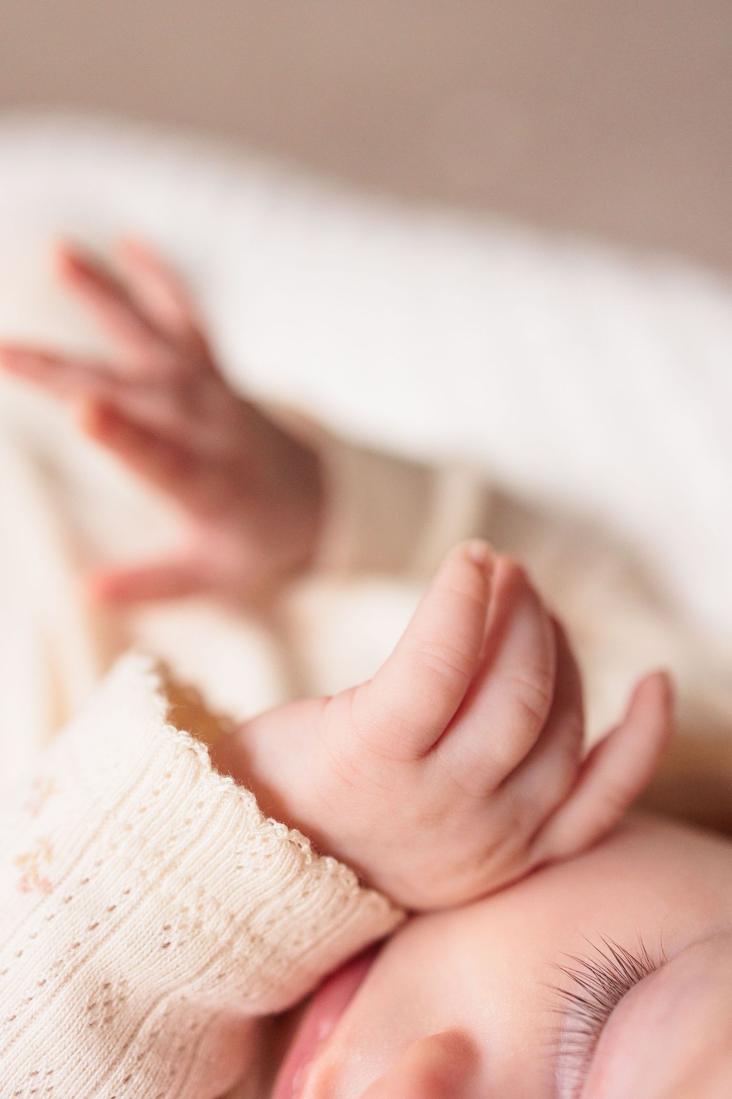 Close-up artistic shots of delicate baby features against soft cream-colored fabric.