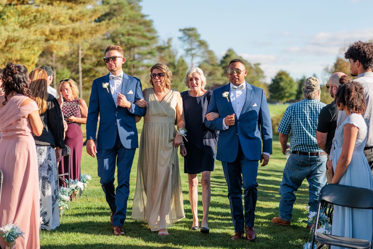 Outdoor wedding celebration with guests in formal attire on a sunny day.