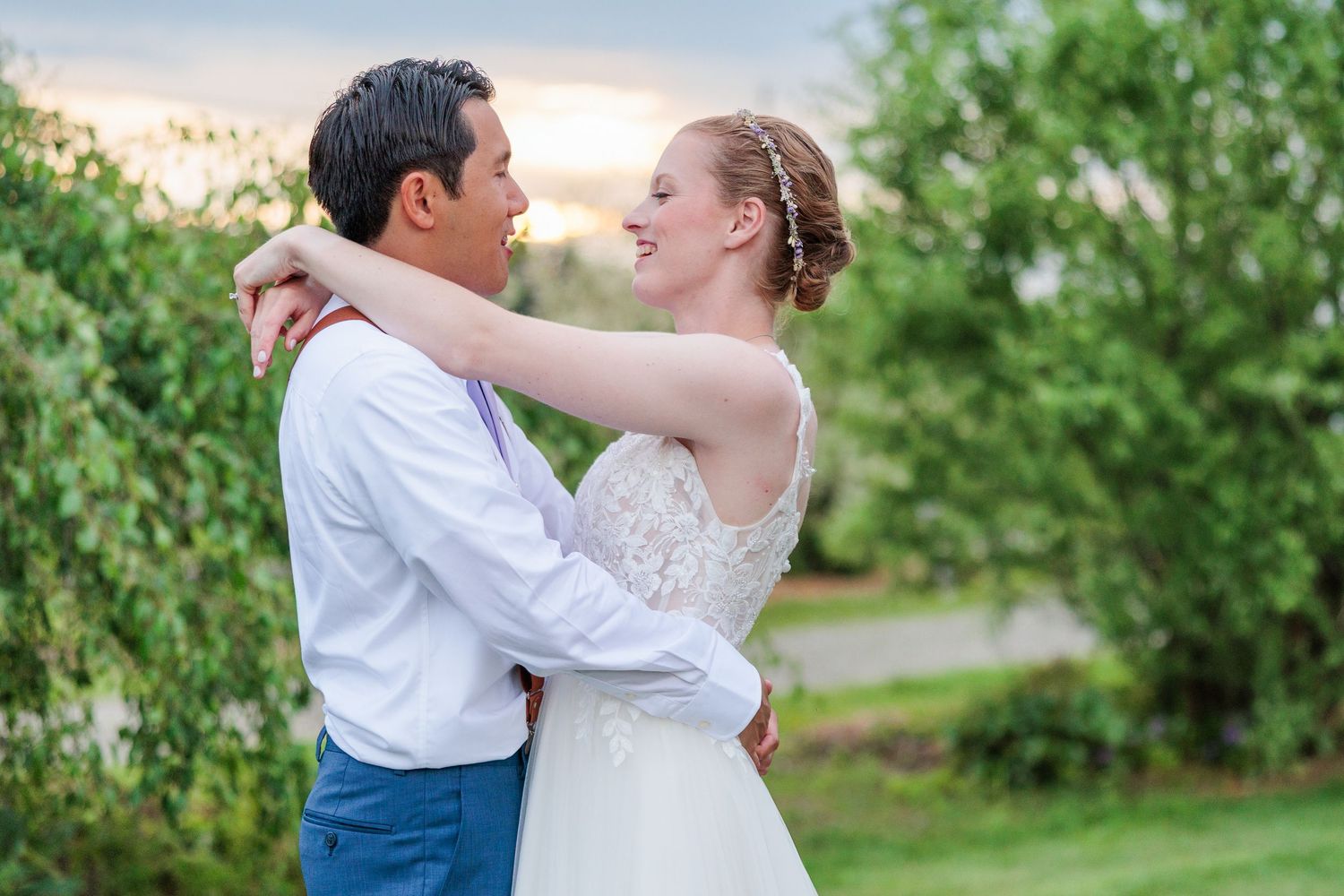 Bride and groom embrace and smile at each other in outdoor garden at sunset.