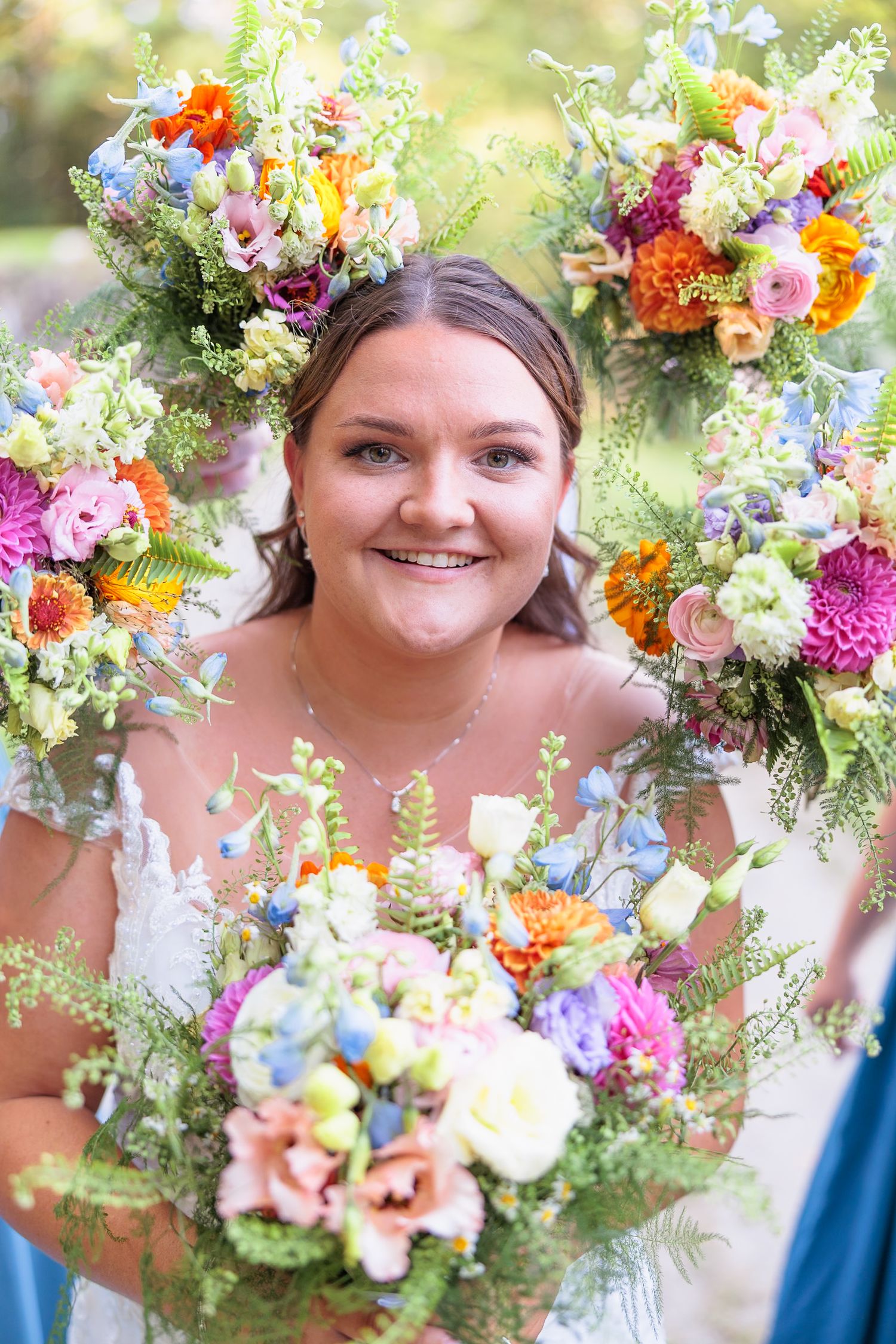 Smiling bride framed by colorful wildflower bouquets in pink, orange, blue, and yellow at her wedding.