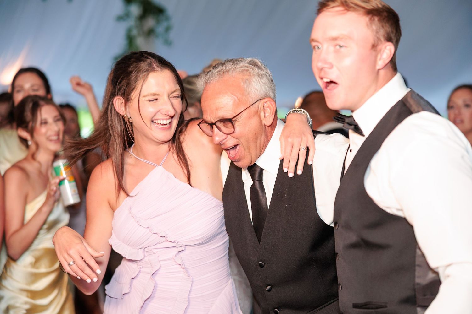 Three wedding guests smiling and laughing together on the dance floor at a reception.