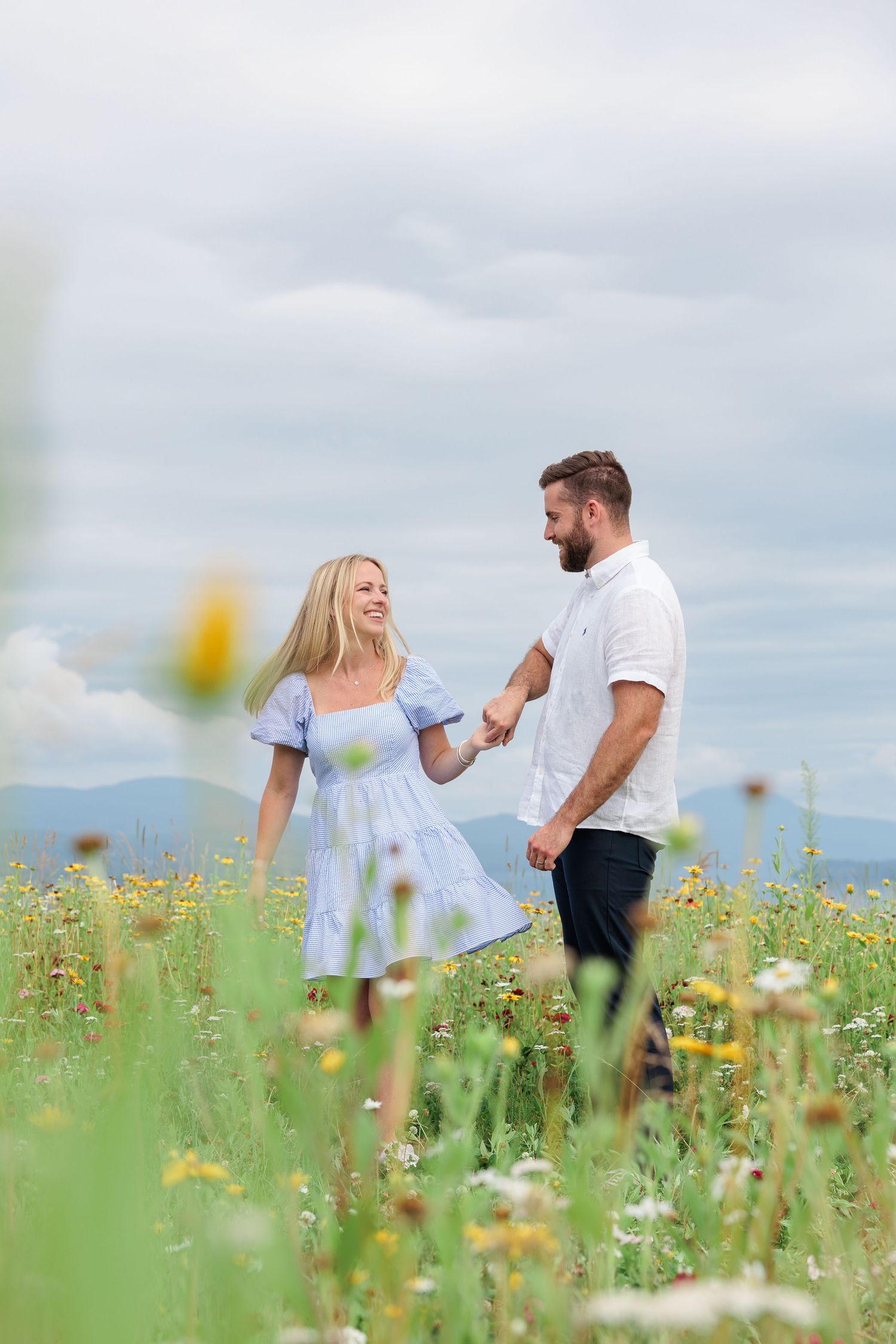 Couple walking hand in hand through a blooming wildflower meadow with scenic mountain views behind them.