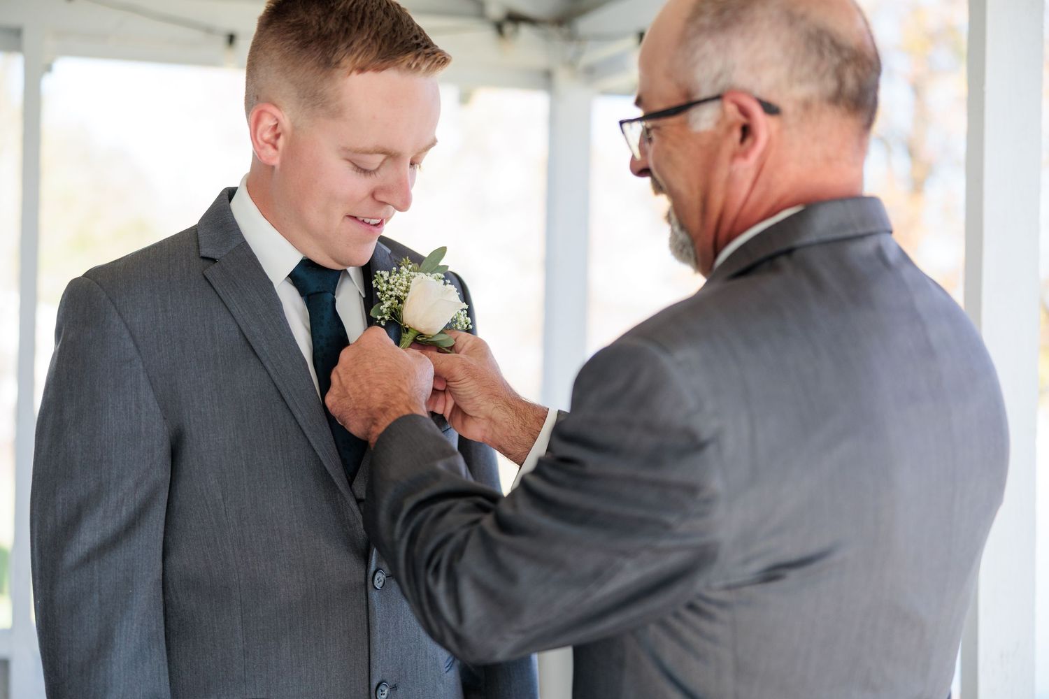 Groomsmen share emotional embraces and adjust boutonnieres while getting ready for a wedding ceremony.
