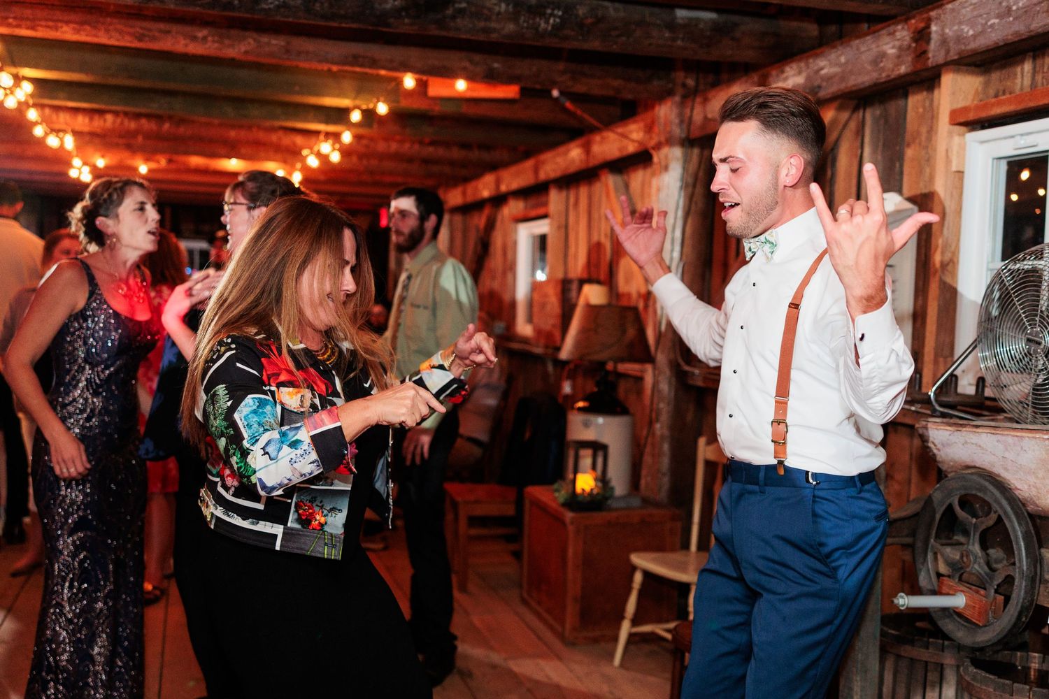 People dancing and celebrating at a rustic barn reception with warm lighting.