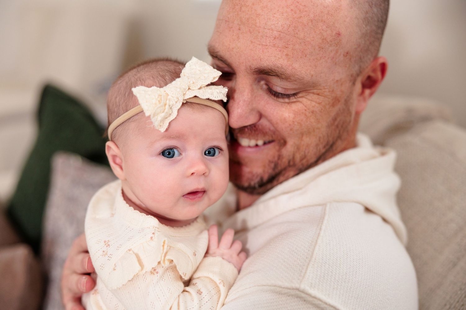 Tender embrace between parent and baby wearing cream colored outfit.