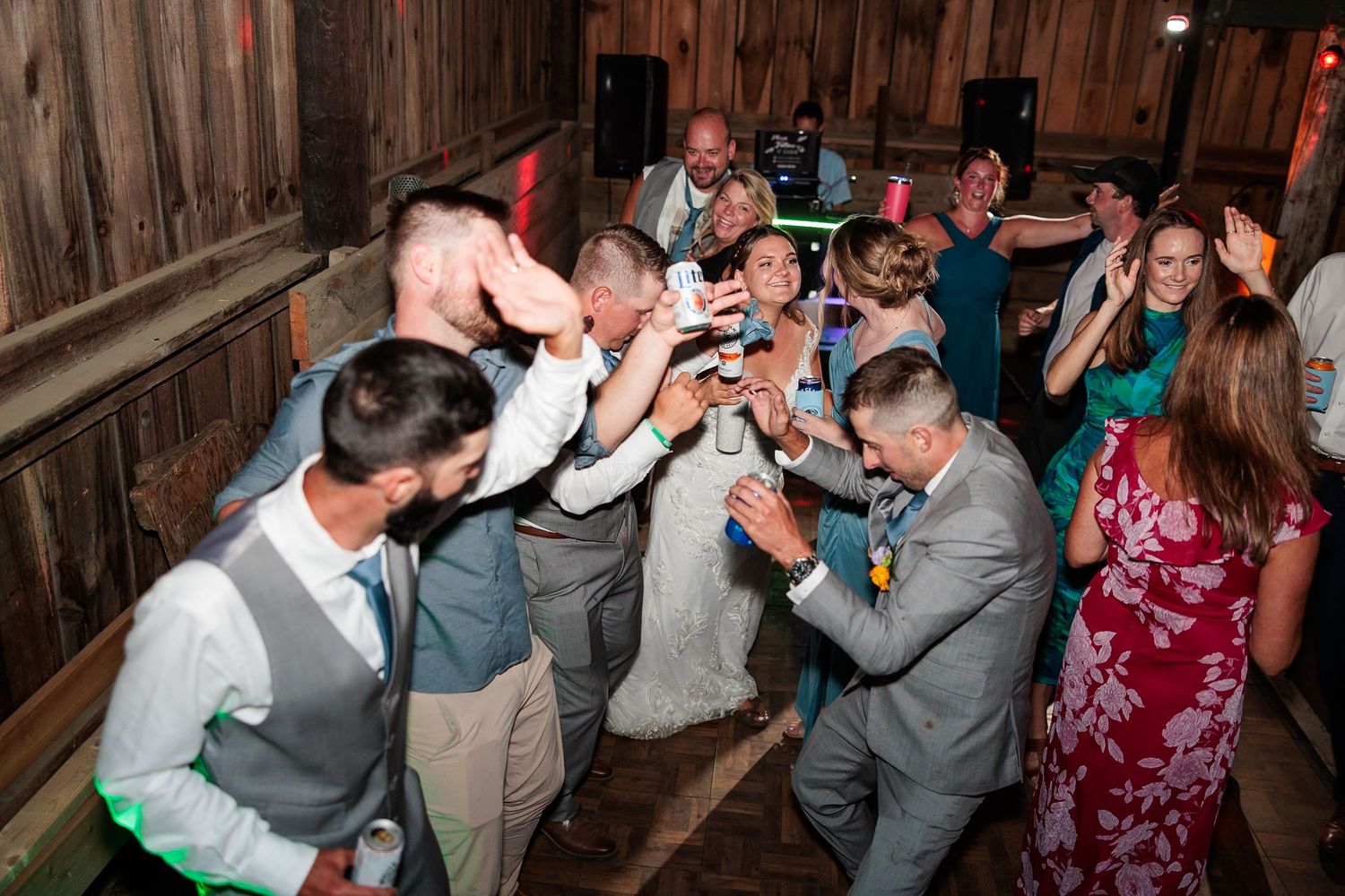 Wedding guests and bridal party gather for lively group celebration on rustic barn dance floor.