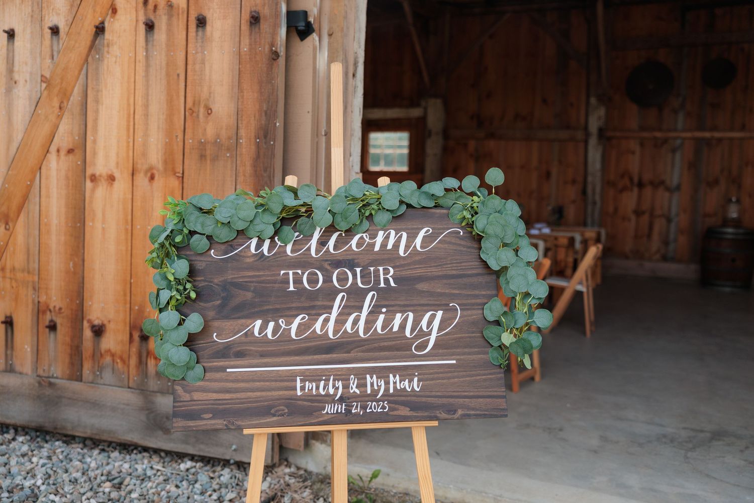 Rustic wooden welcome wedding sign decorated with eucalyptus greenery inside a barn venue.