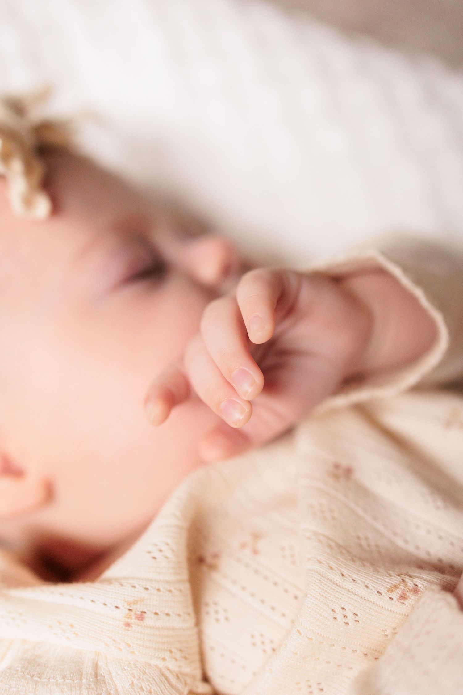 A sleeping baby's tiny hand rests peacefully against soft cream-colored lace fabric.