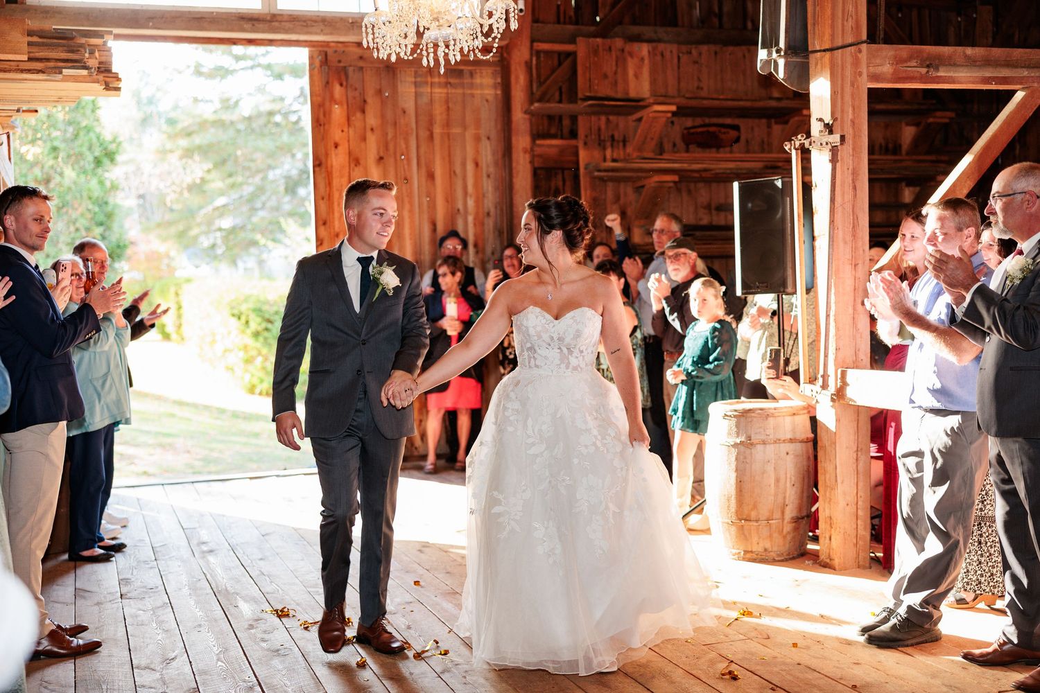 Bride and groom making grand entrance into rustic barn wedding reception to cheering guests.