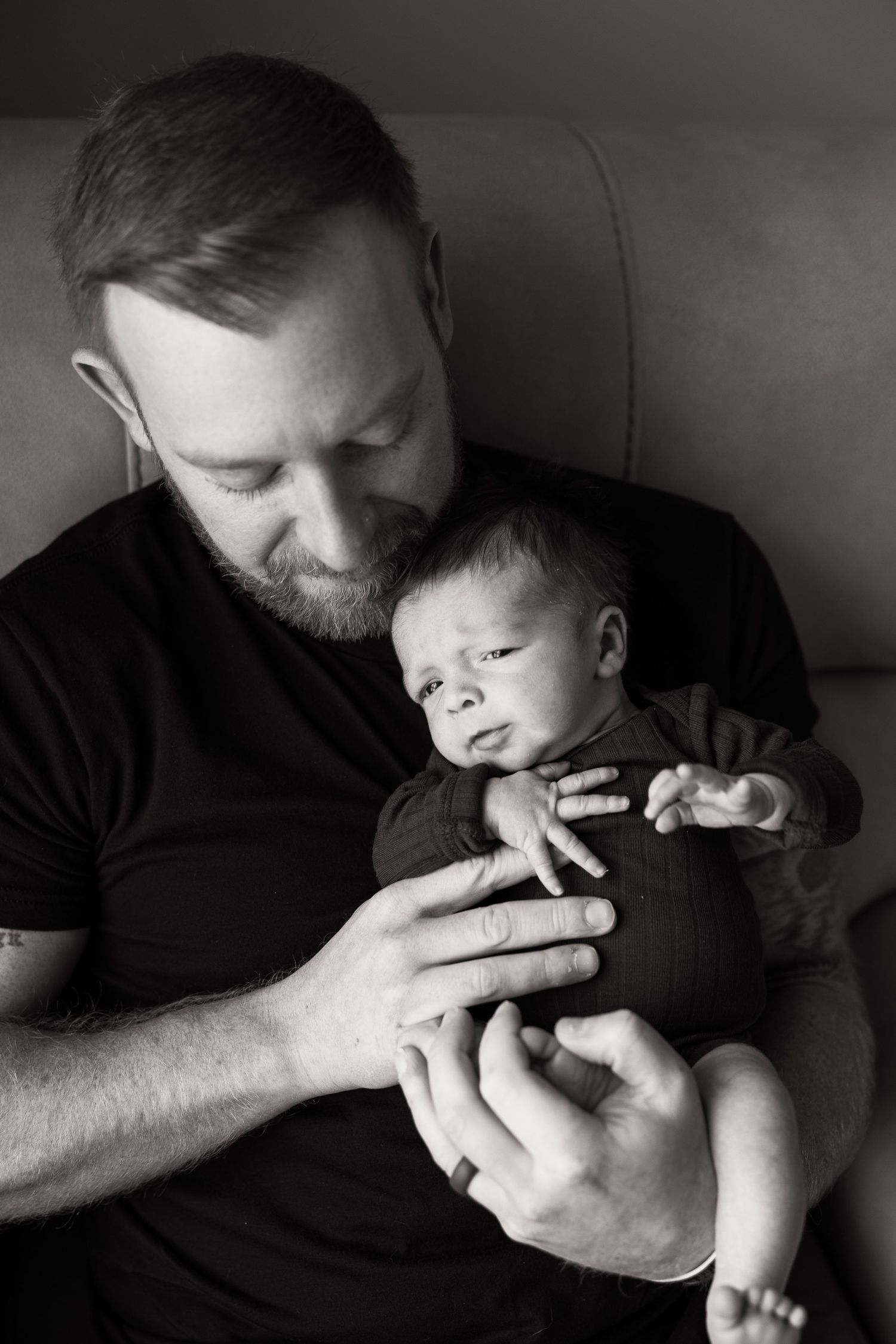 Black and white portrait of a bearded father gently cradling his alert newborn baby.