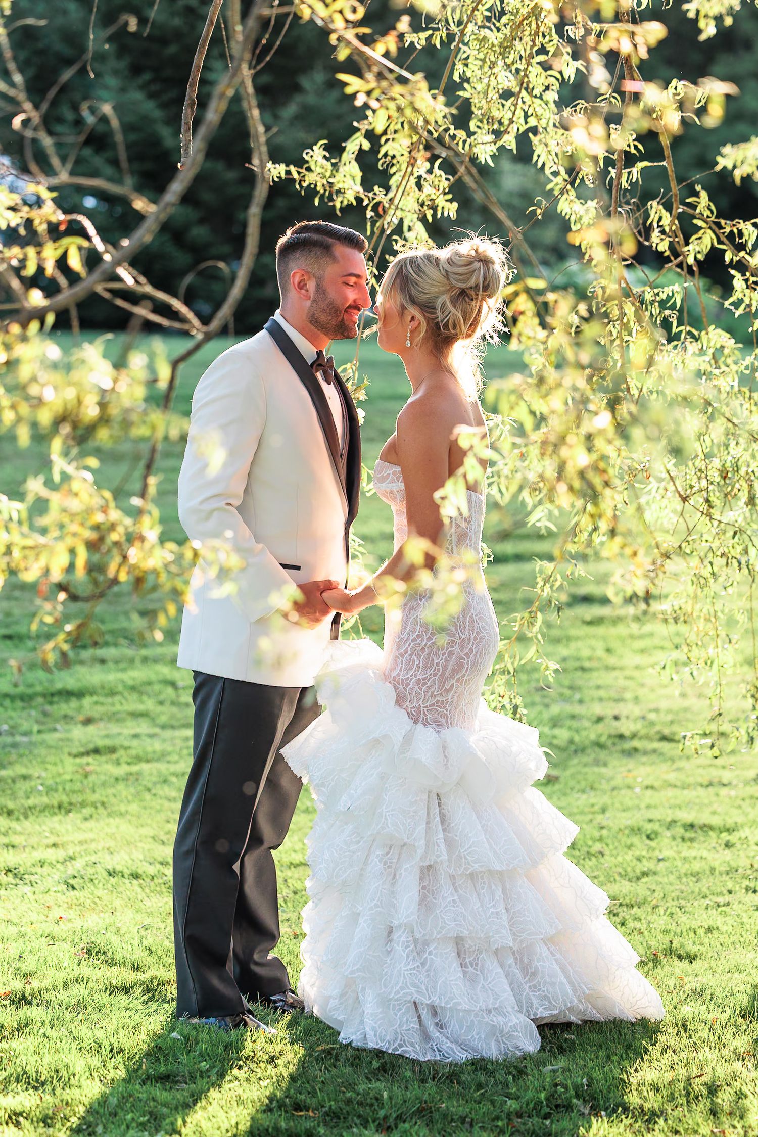 Bride and groom holding hands and gazing at each other outdoors under golden sunlit trees during wedding portrait session.