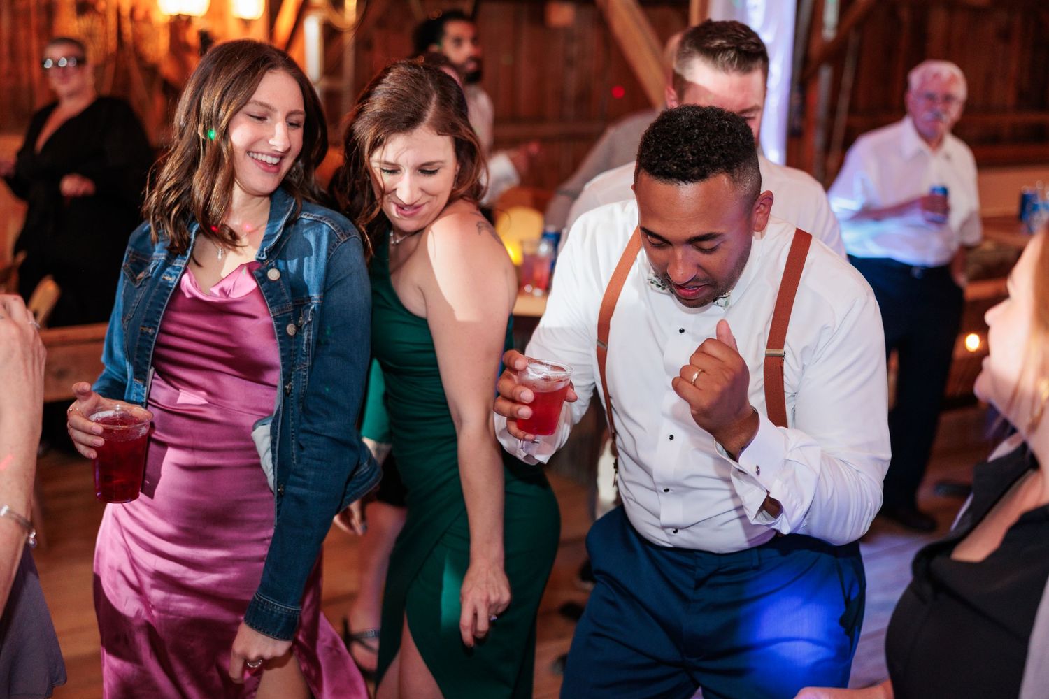 Guests dancing and celebrating at a barn reception with warm lighting and rustic decor.