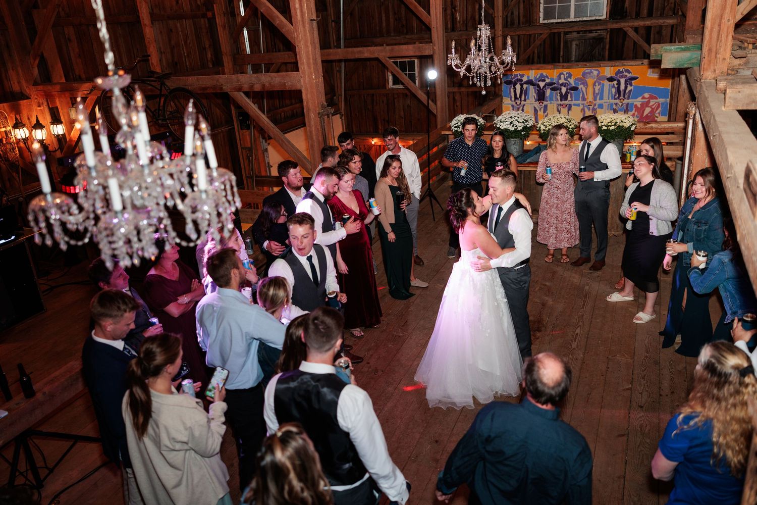 Wedding guests celebrate on a dimly lit dance floor inside a rustic barn venue.