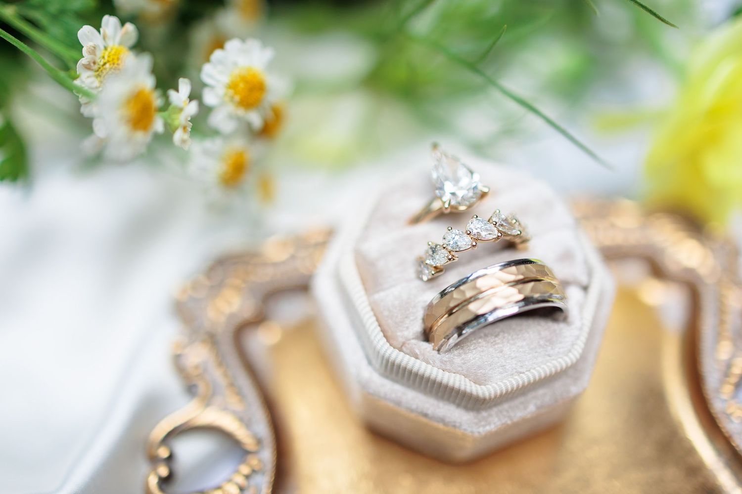 Close-up of diamond engagement ring and gold wedding bands displayed in a velvet ring box.