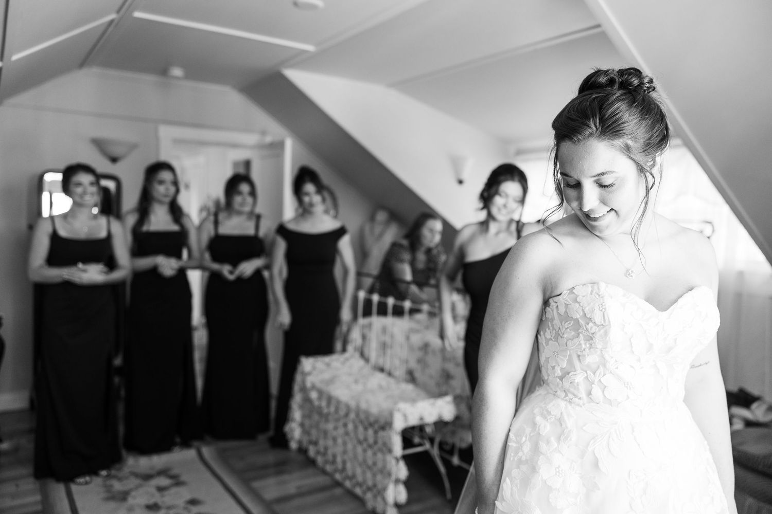 Black and white photo of bridesmaids in black dresses reacting to bride in wedding gown.
