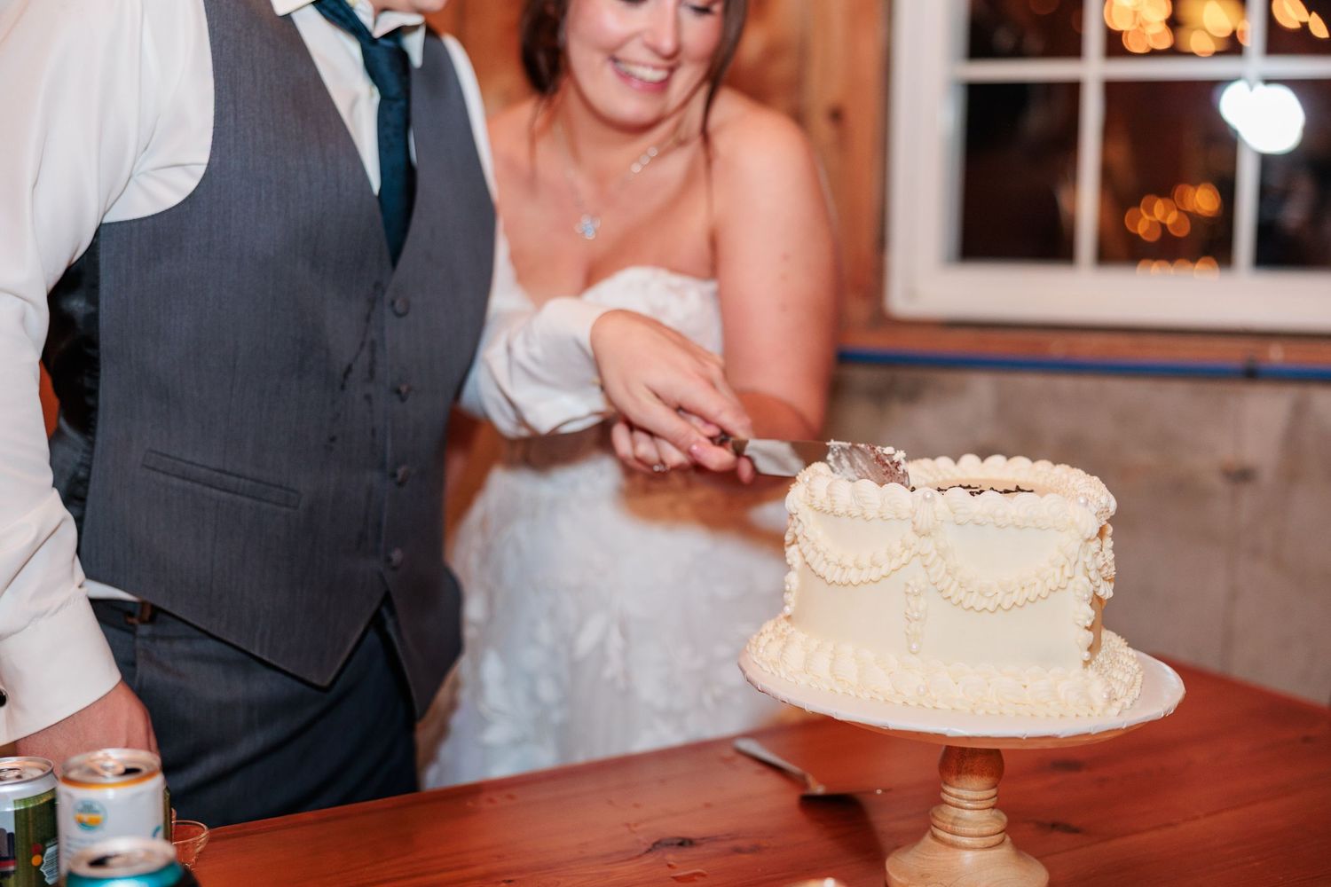 Bride and groom cut their elegant white wedding cake together during their barn reception.