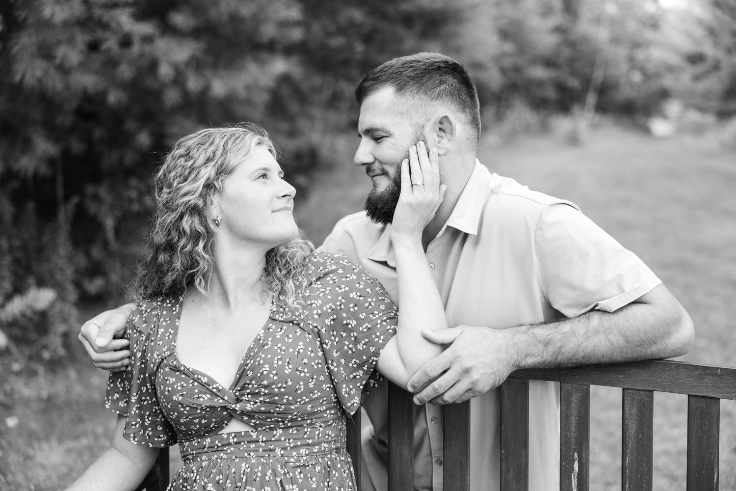 Black and white photo of a couple sitting on a bench, woman touching mans bearded face tenderly.
