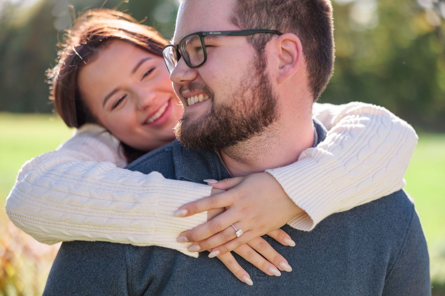 Happy woman hugging her fiance outdoors showing her engagement ring in autumn sunlight.